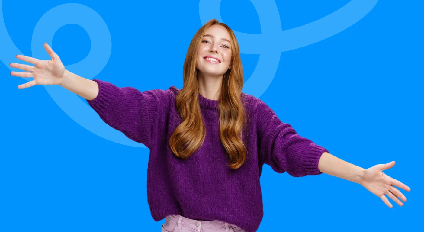 Smiling woman in a purple jumper opening her arms wide in welcome.