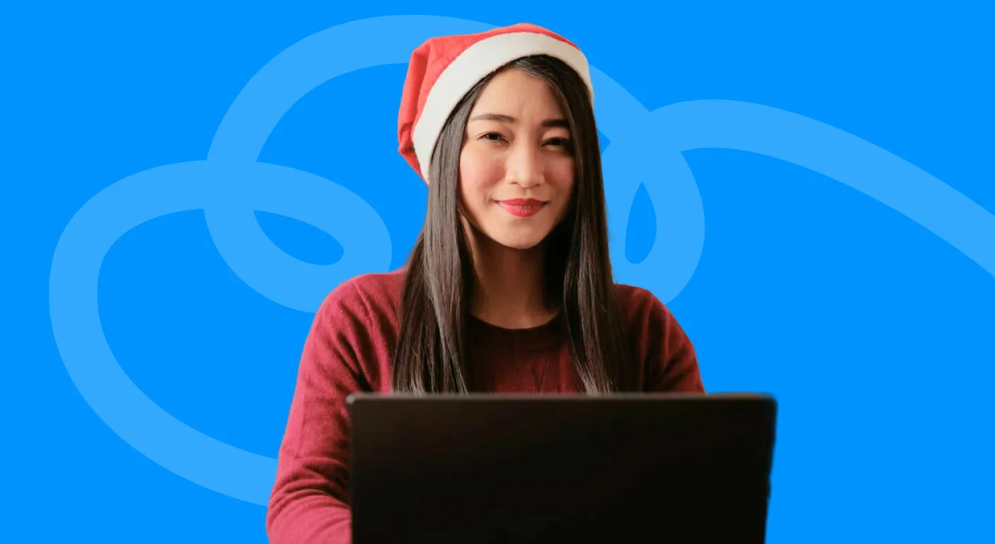 Woman wearing a Santa hat smiling at her laptop while planning Christmas email marketing campaigns.