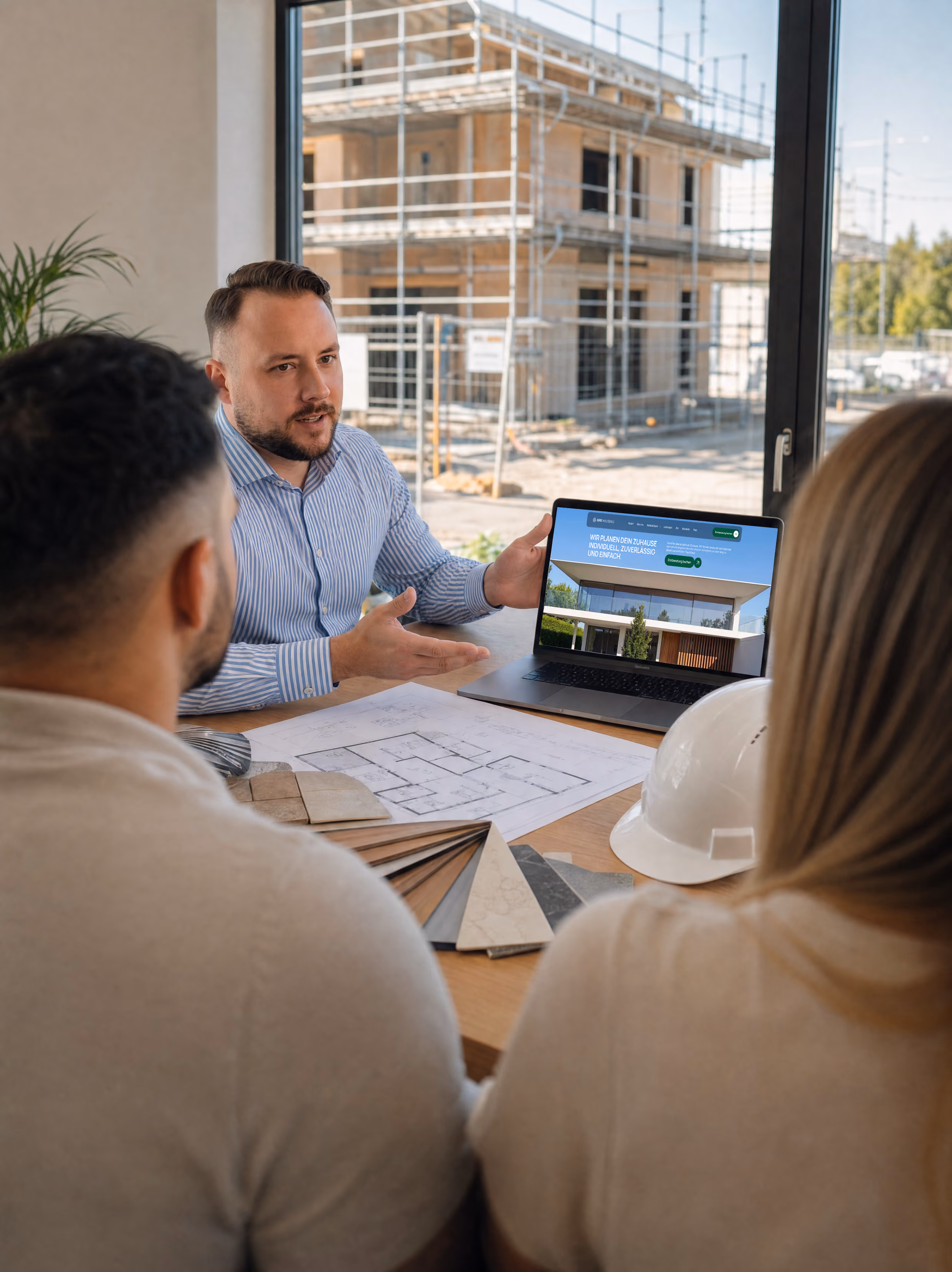 Ein Architekt zeigt einem Paar am Tisch Hauspläne und ein modernes Hausdesign auf einem Laptop.