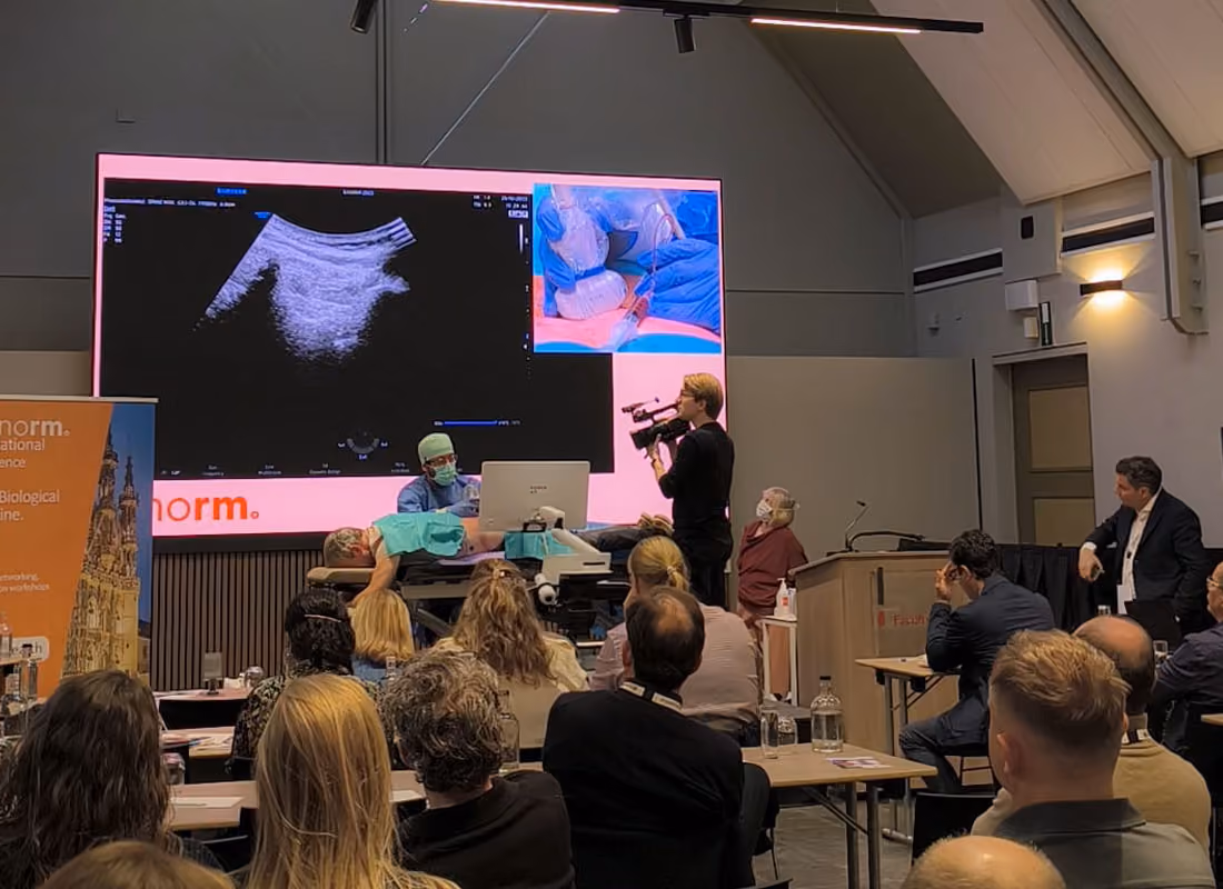 Medical professional demonstrates ultrasound on patient as audience watches in a conference room.