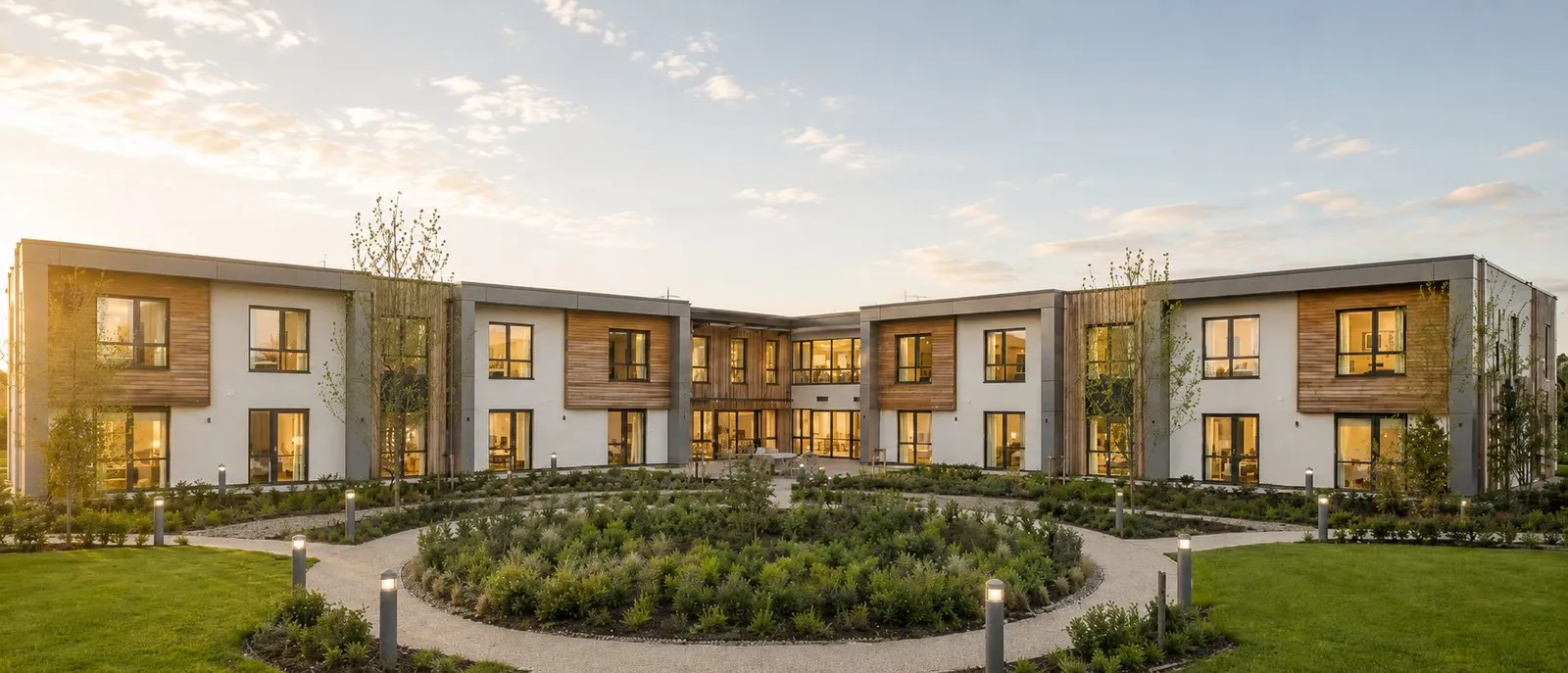 A completed courtyard care home in timber and render, set in landscaped grounds at dusk