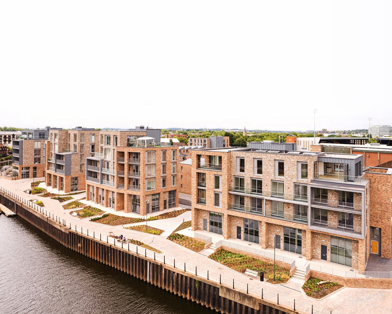 Aerial photograph of Muller Yard, Nottingham: brick apartment blocks and townhouses stepping along a new quayside walk on the bank of the River Trent.
