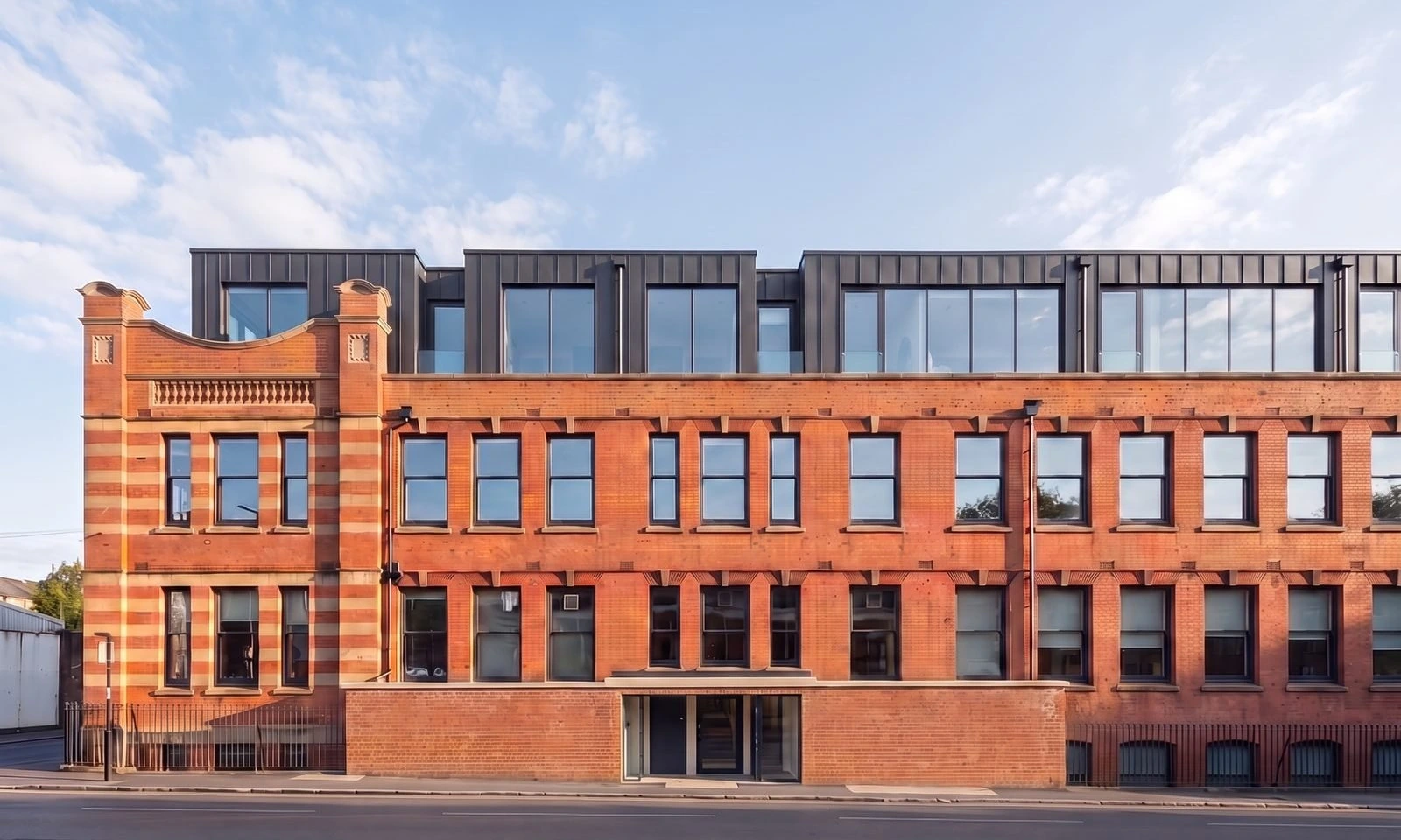 Enhanced photograph of the converted 1906 Former Challenge Cycle Works at Foleshill Road, Coventry: the retained red-brick and terracotta facade with its ornate gable below the new dark zinc-clad top storey added by the conversion