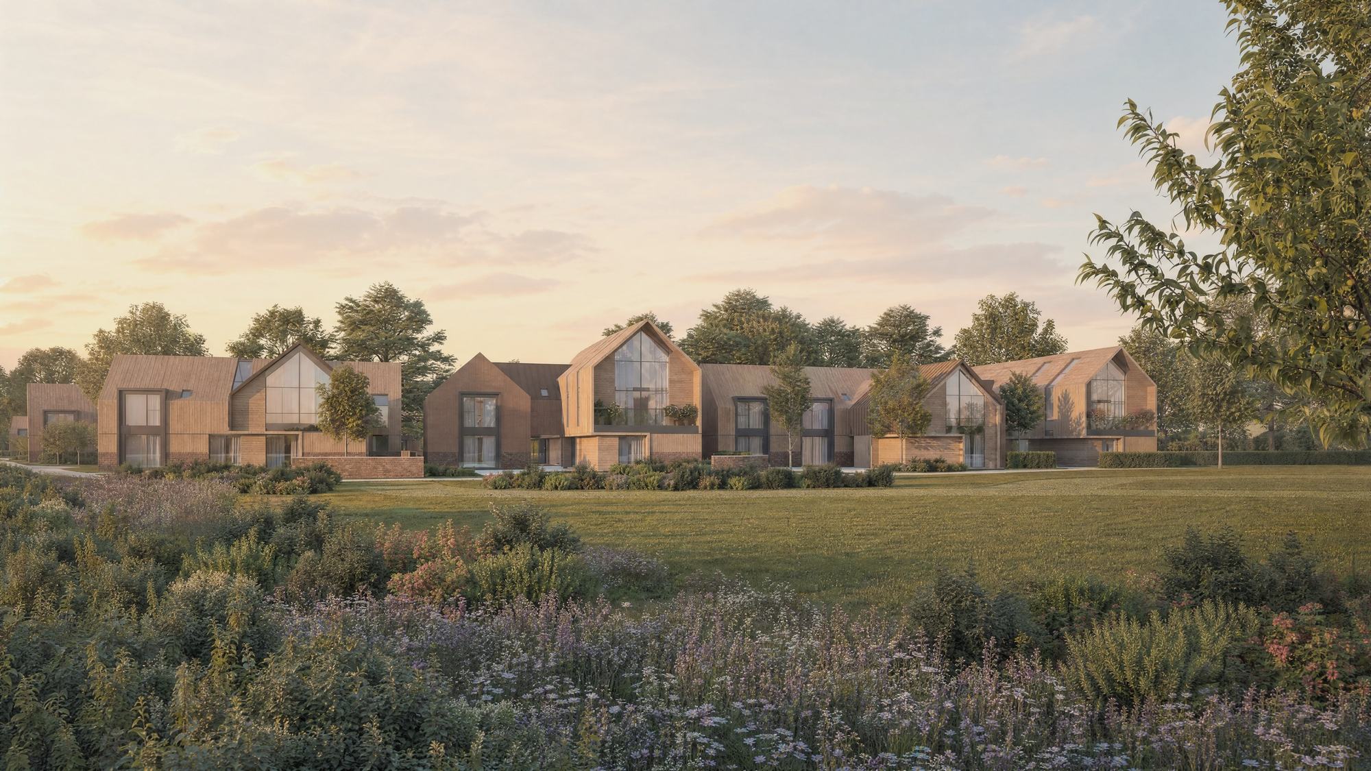 Visualisation of Inwoods Park, Rugby, designed by Rickett Architects: a row of contemporary agrarian houses with standing-seam zinc roofs, timber cladding, brick plinths and full-height gable glazing, seen across a wildflower meadow in soft early-morning light