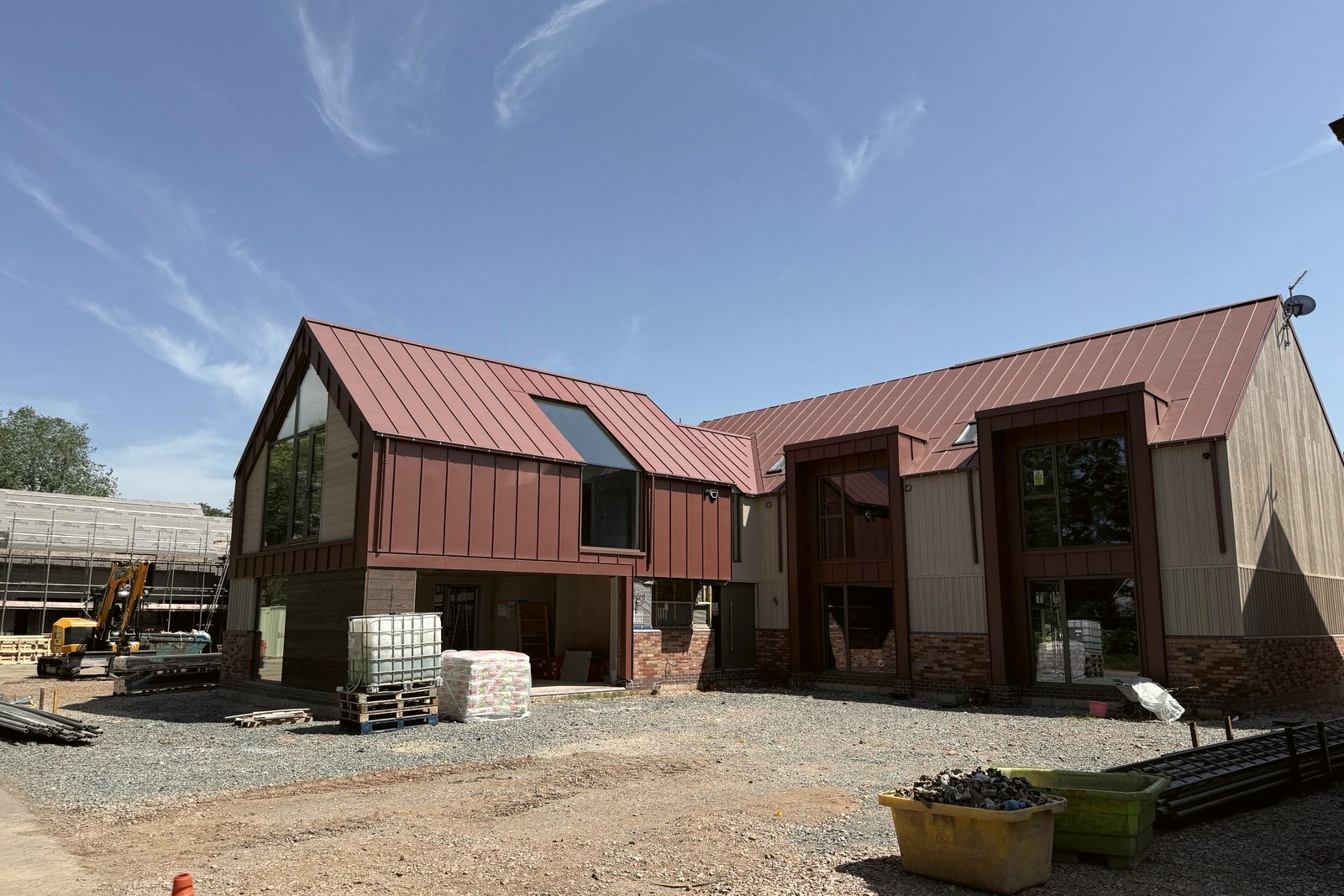 Photograph of a house under construction at Inwoods Park, Rugby, June 2026: the standing-seam zinc roof and zinc-clad dormers over timber cladding and a brick plinth, nearly complete