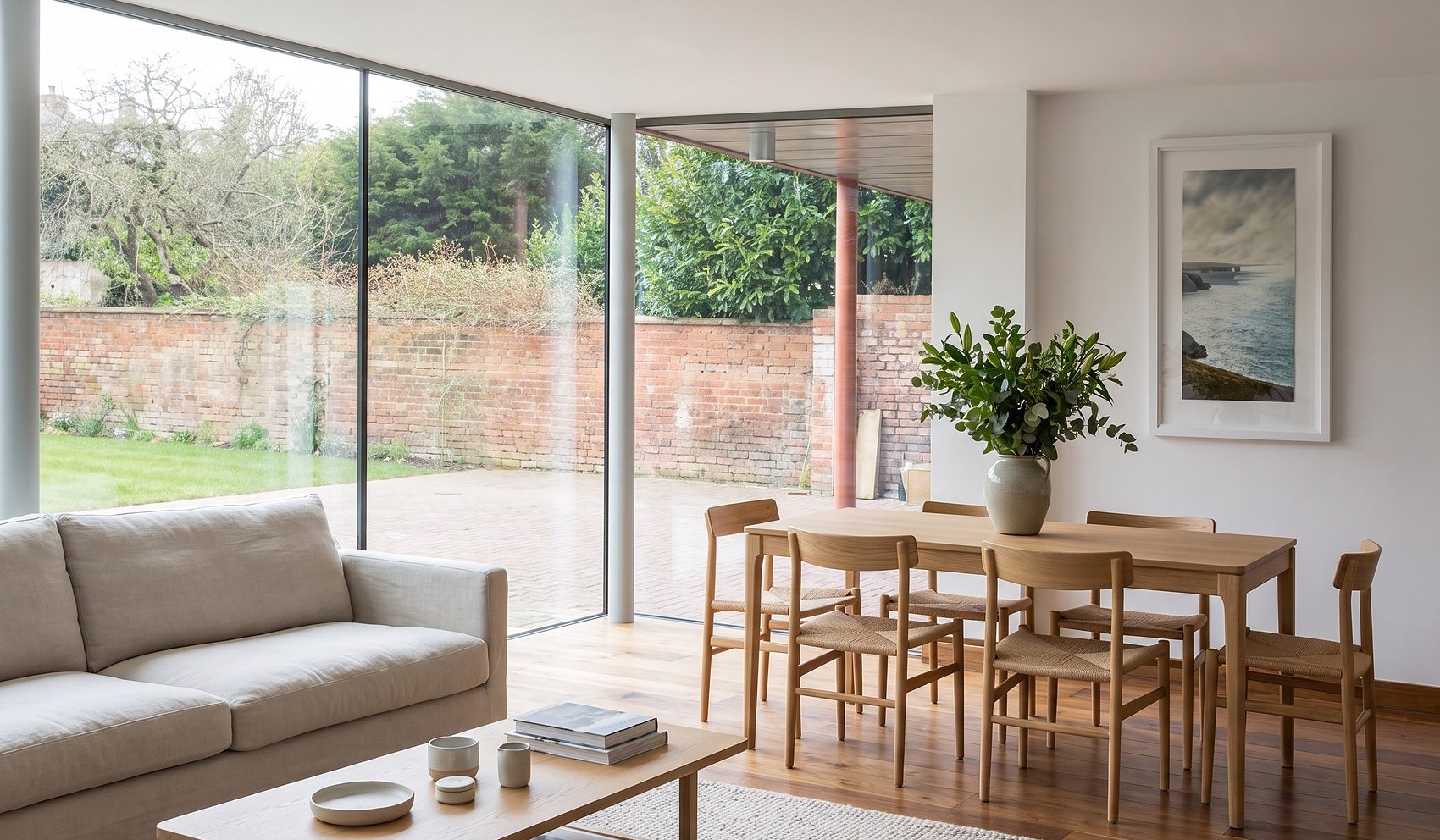 Inside the completed house on Kenilworth Road, Royal Leamington Spa: an open living and dining space with a walnut floor, opening through full height corner glazing to the walled garden and lawn beyond