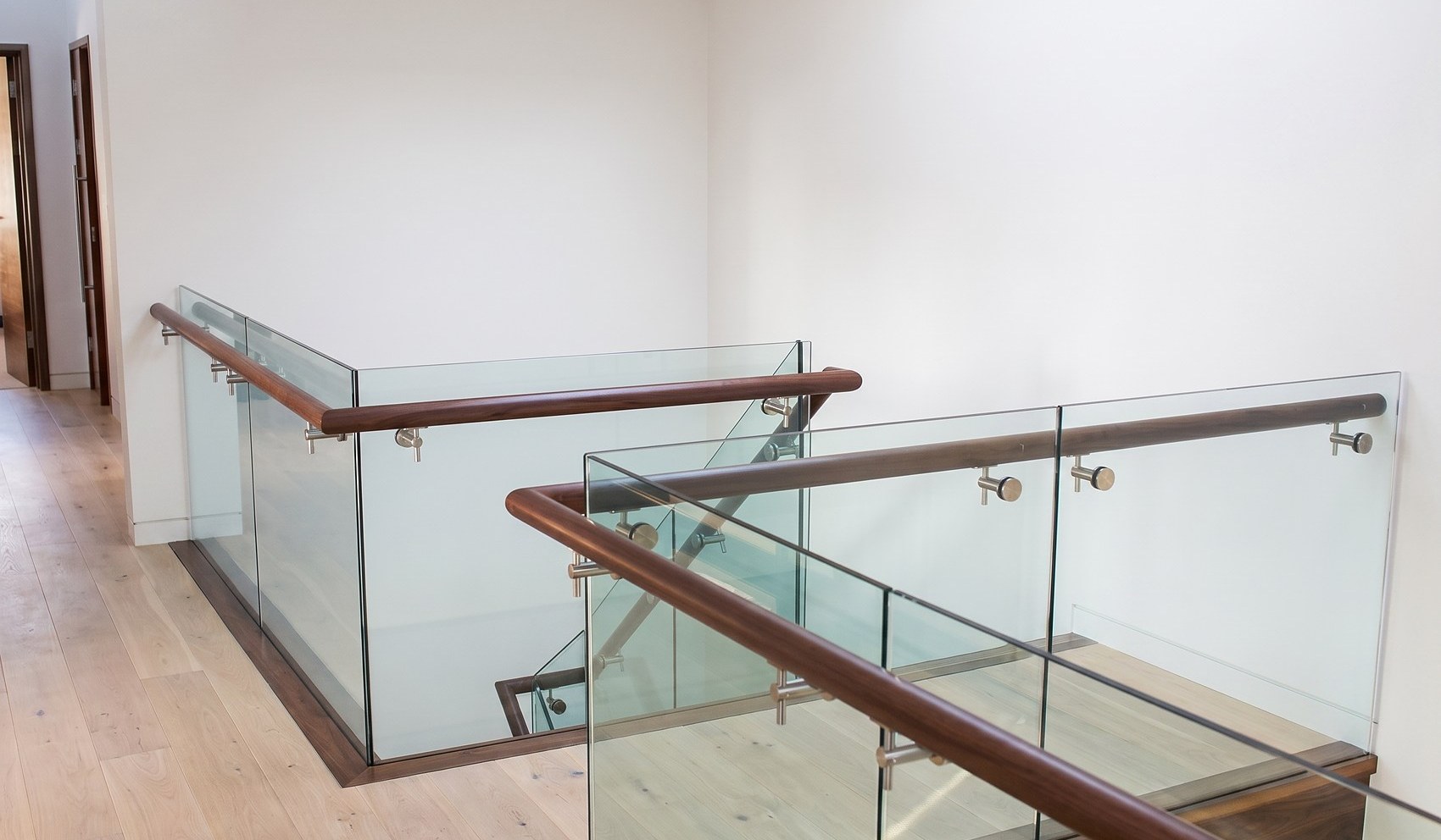 The bespoke stair and first floor landing in the completed house on Kenilworth Road, Royal Leamington Spa: a walnut handrail and solid walnut treads with a frameless glass balustrade, on a pale timber floor