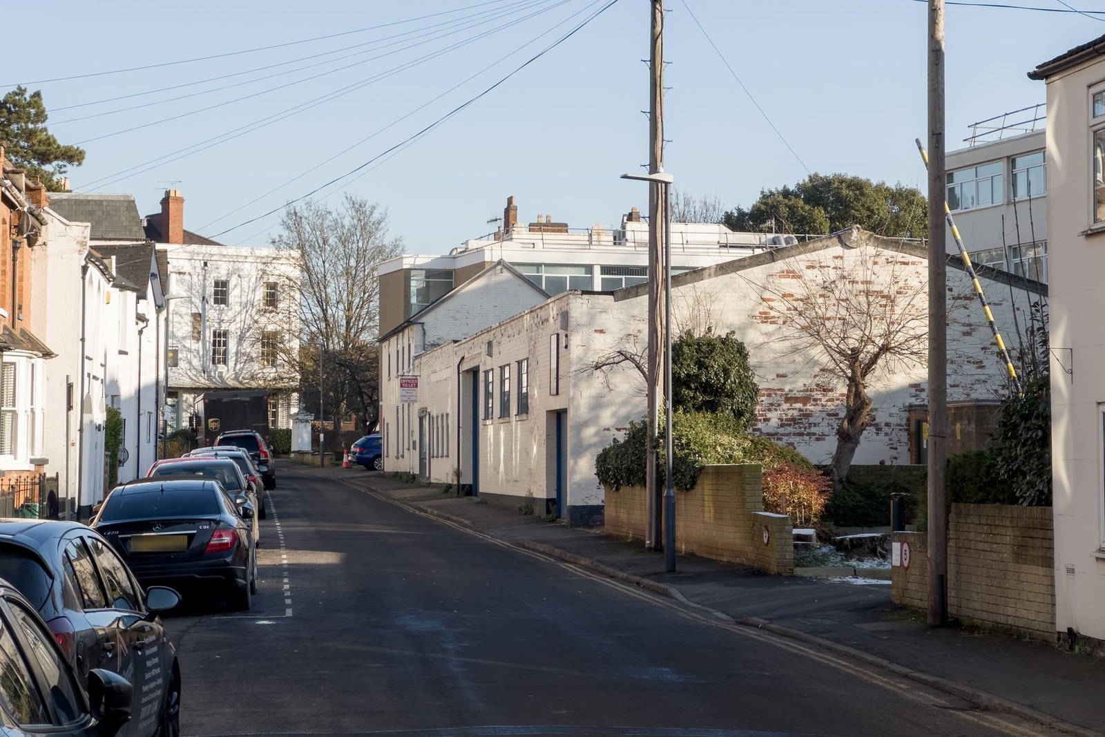 The site as found: a run-down two-storey commercial building on Cross Street with boarded and blanked ground-floor openings and an offices to let board, seen down the street past parked cars and a lamp post.
