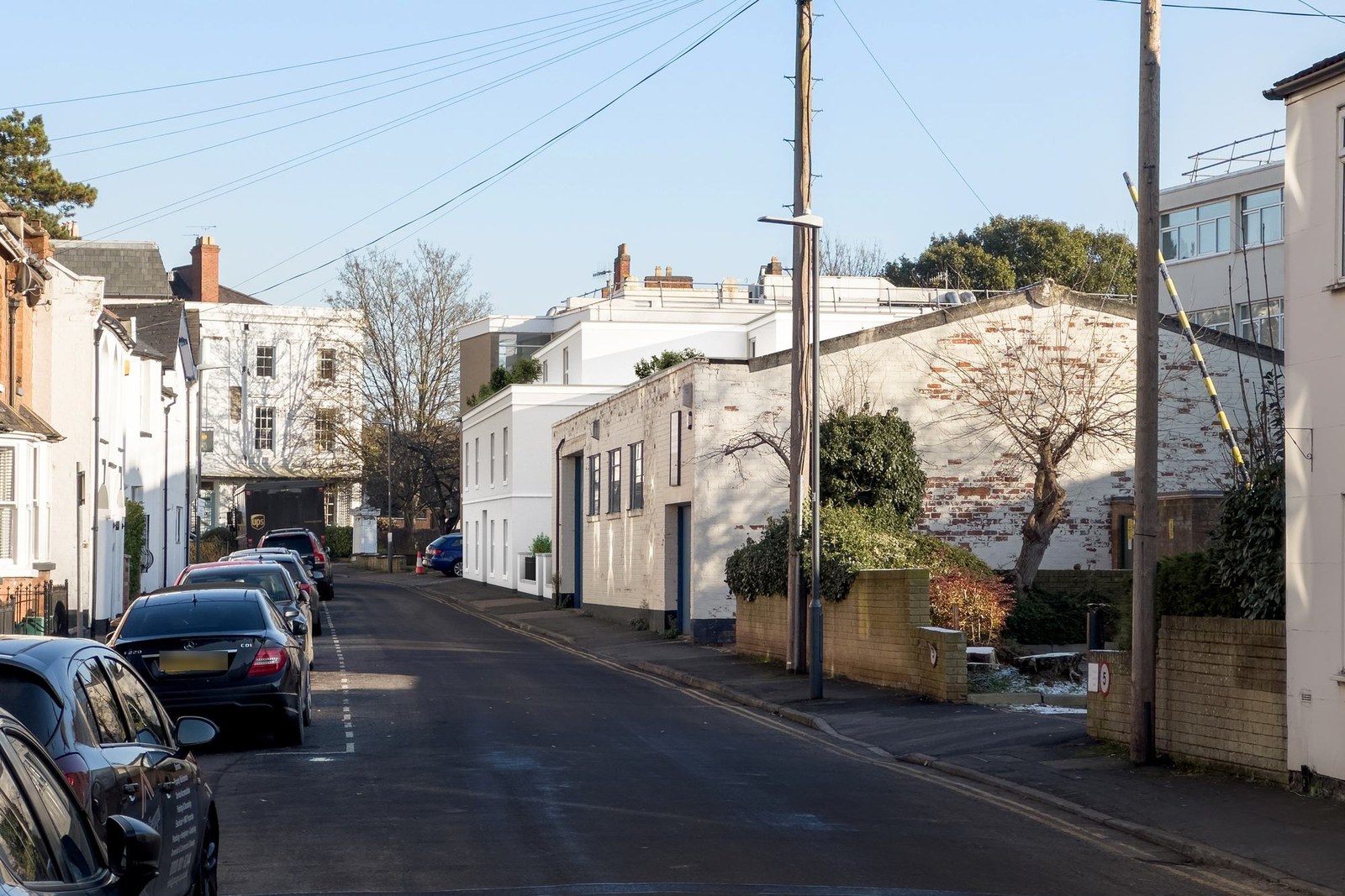 A visualisation of the consented scheme from the same standpoint: a three-storey white-rendered building with a Regency parapet, sliding-sash windows on stone cills and a set-back top floor, with the same parked cars, lamp post and boundary wall in front of it.