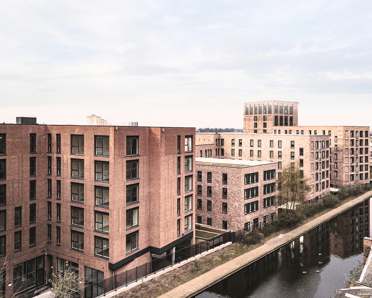Enhanced photograph of the completed brick apartment building at Cliveland Street, Birmingham, standing on the canal towpath with the wider neighbourhood beyond.