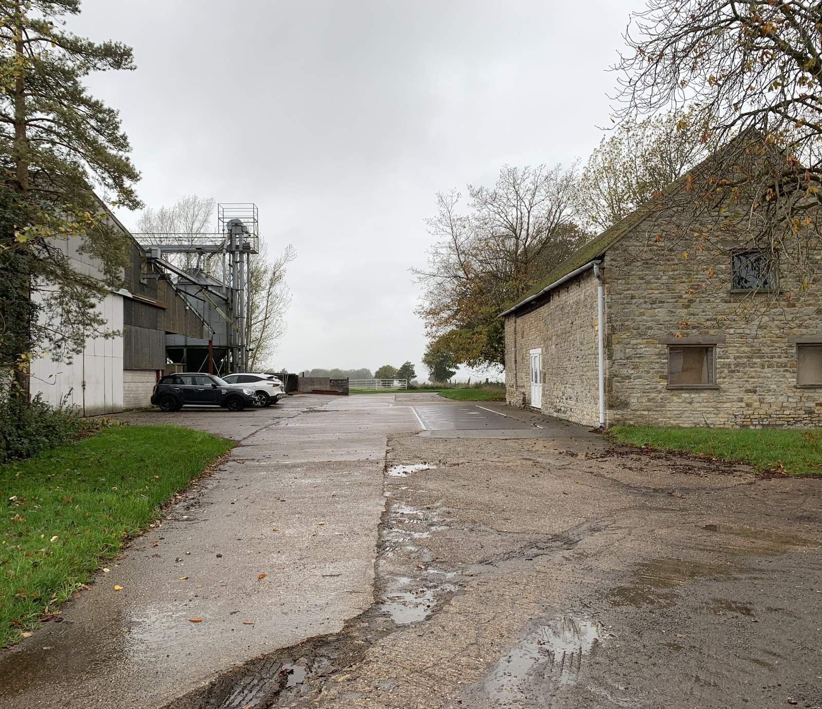 The working farmyard as found, in colour: the stone barn on the right, the metal-clad grain plant and silo tower on the left, and the wet concrete yard between them