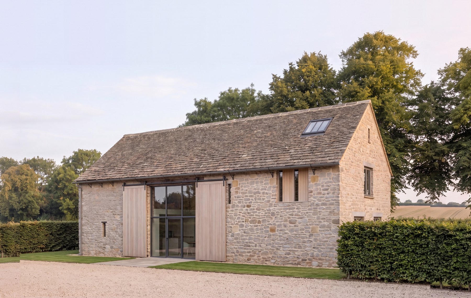 A redundant white lias stone barn consented as a single house, seen across the gravel yard under open evening sky