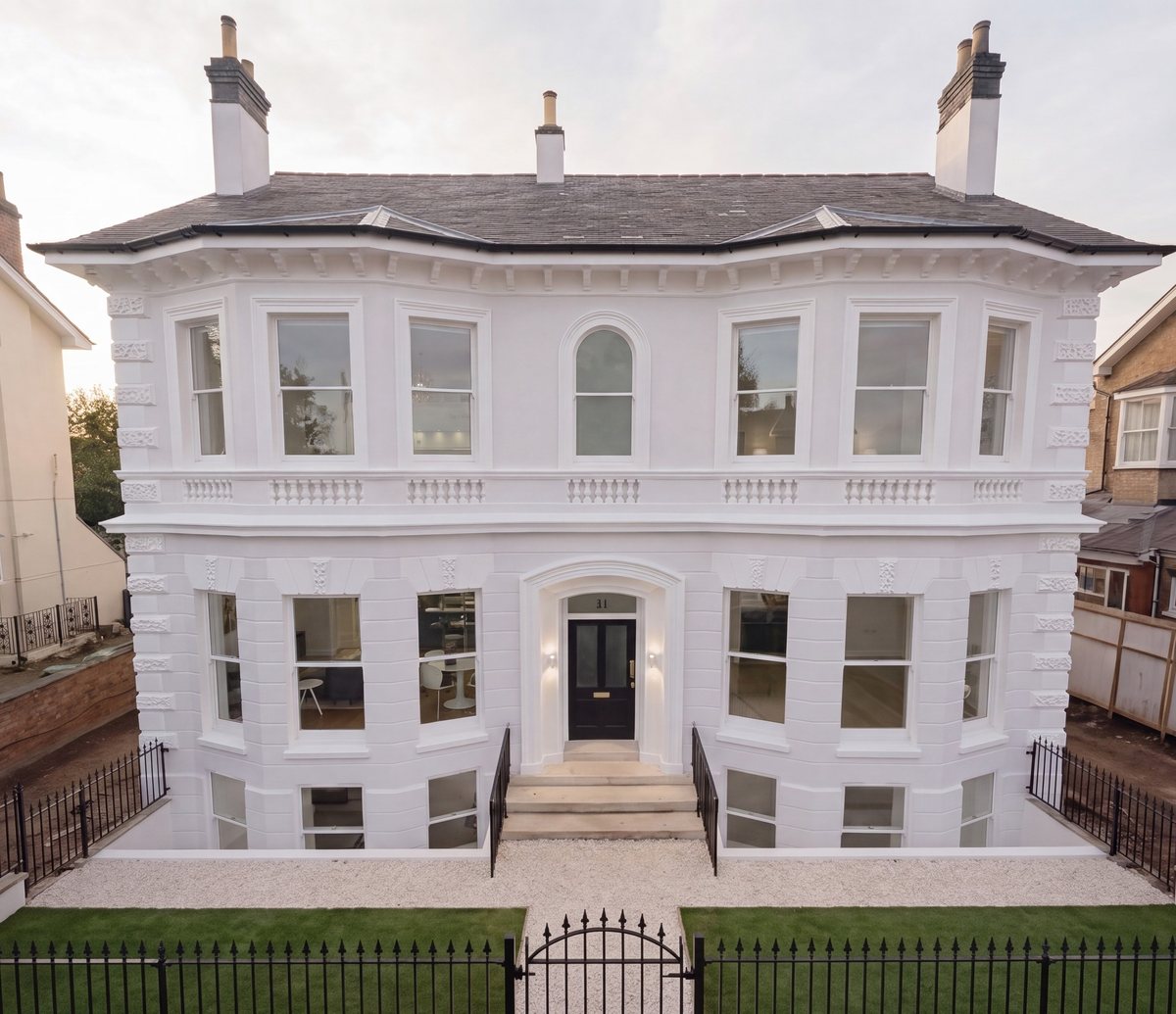 Photograph of the restored period villa at Victoria Court, Leamington Spa: a three-storey white rendered house with canted bay windows, a balustraded band at first floor, a classical porch and door, black railings and a clipped lawn to the street