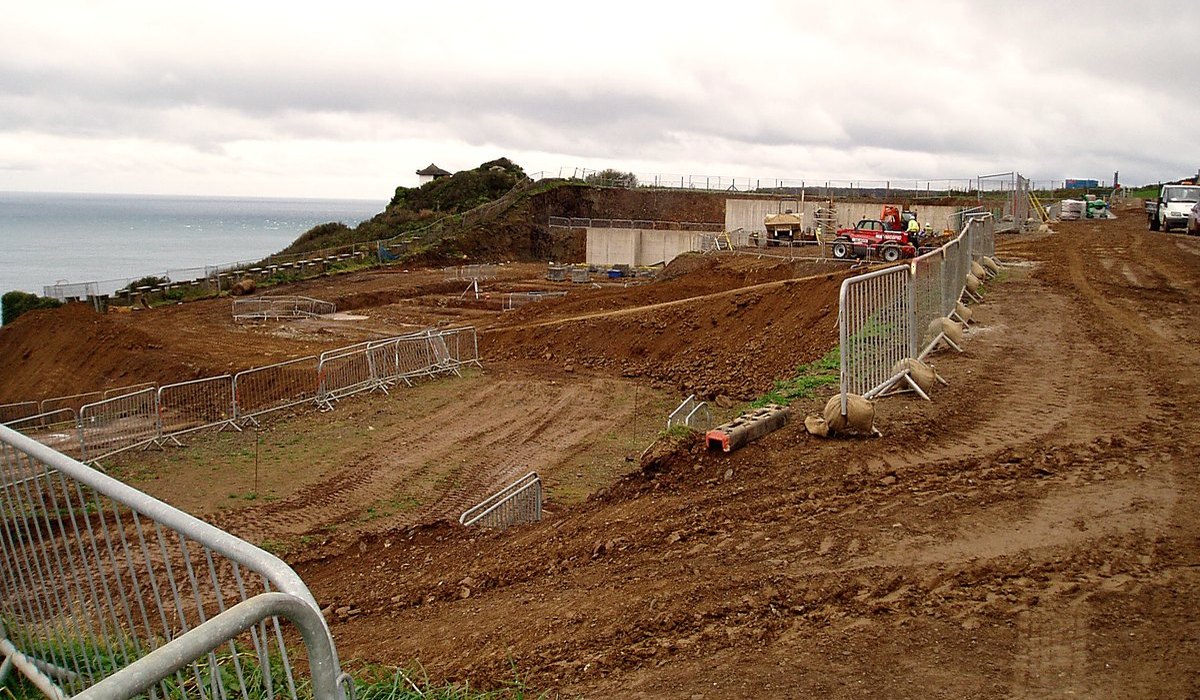 Photograph of the Gara Rock cliff-top site under construction in 2008, the sea beyond: excavated terraces and the first concrete retaining structures cut into the falling headland