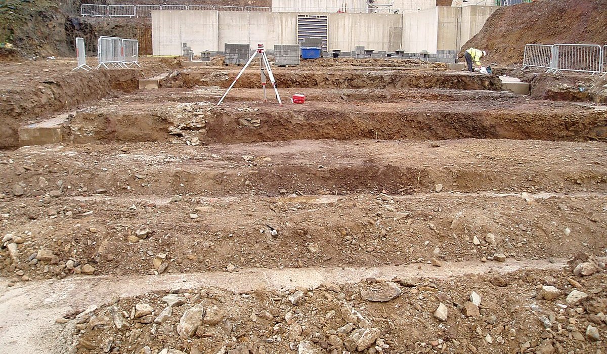 Photograph of foundations and the in-situ concrete retaining wall at Gara Rock under construction in 2008, with a surveyor's level set up on the cut platform