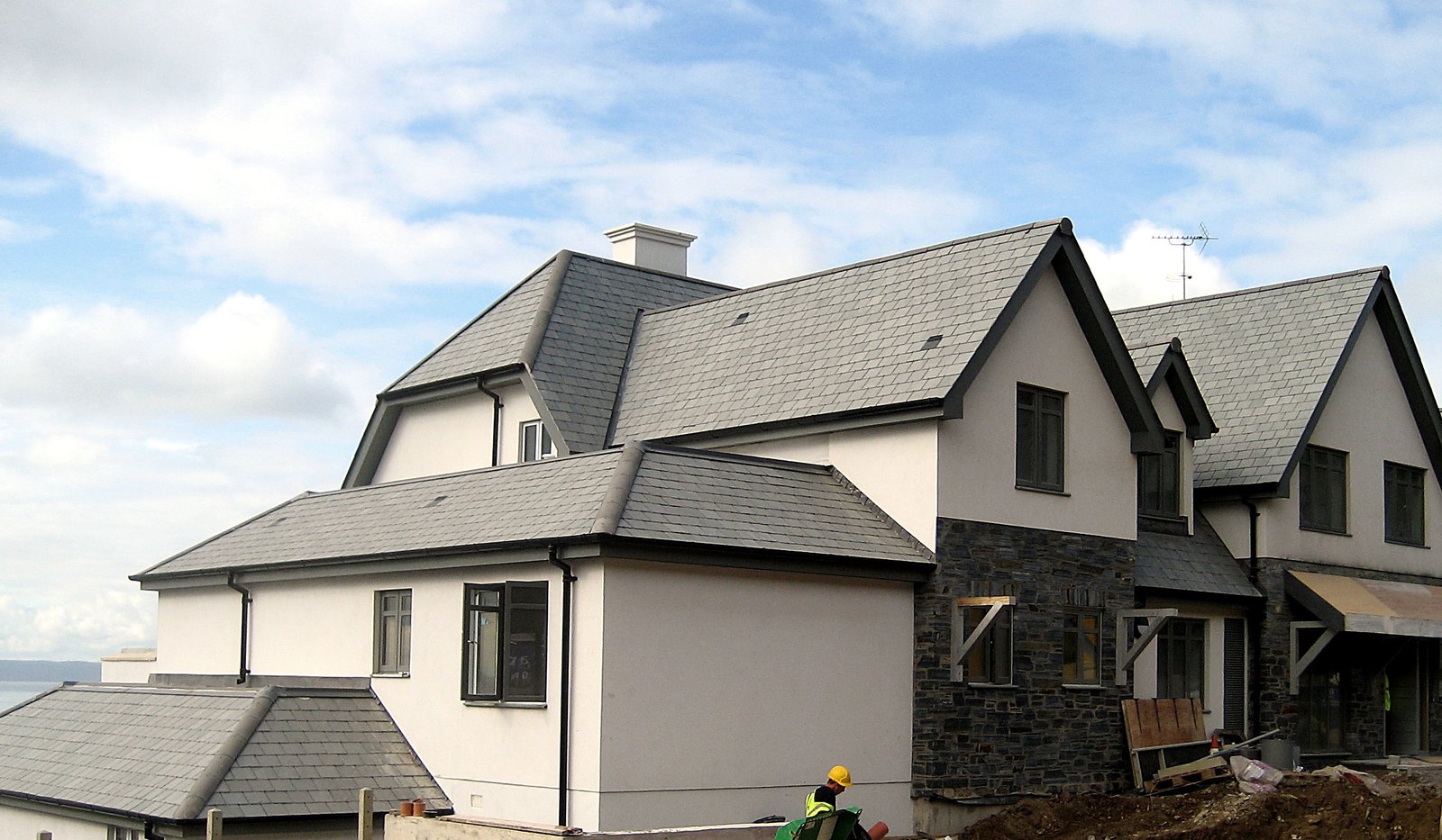 Photograph of Ocean Point in its final weeks on site, September 2009: the gabled, slate-roofed building in fresh render and natural stone, a worker on the terrace and the sea beyond