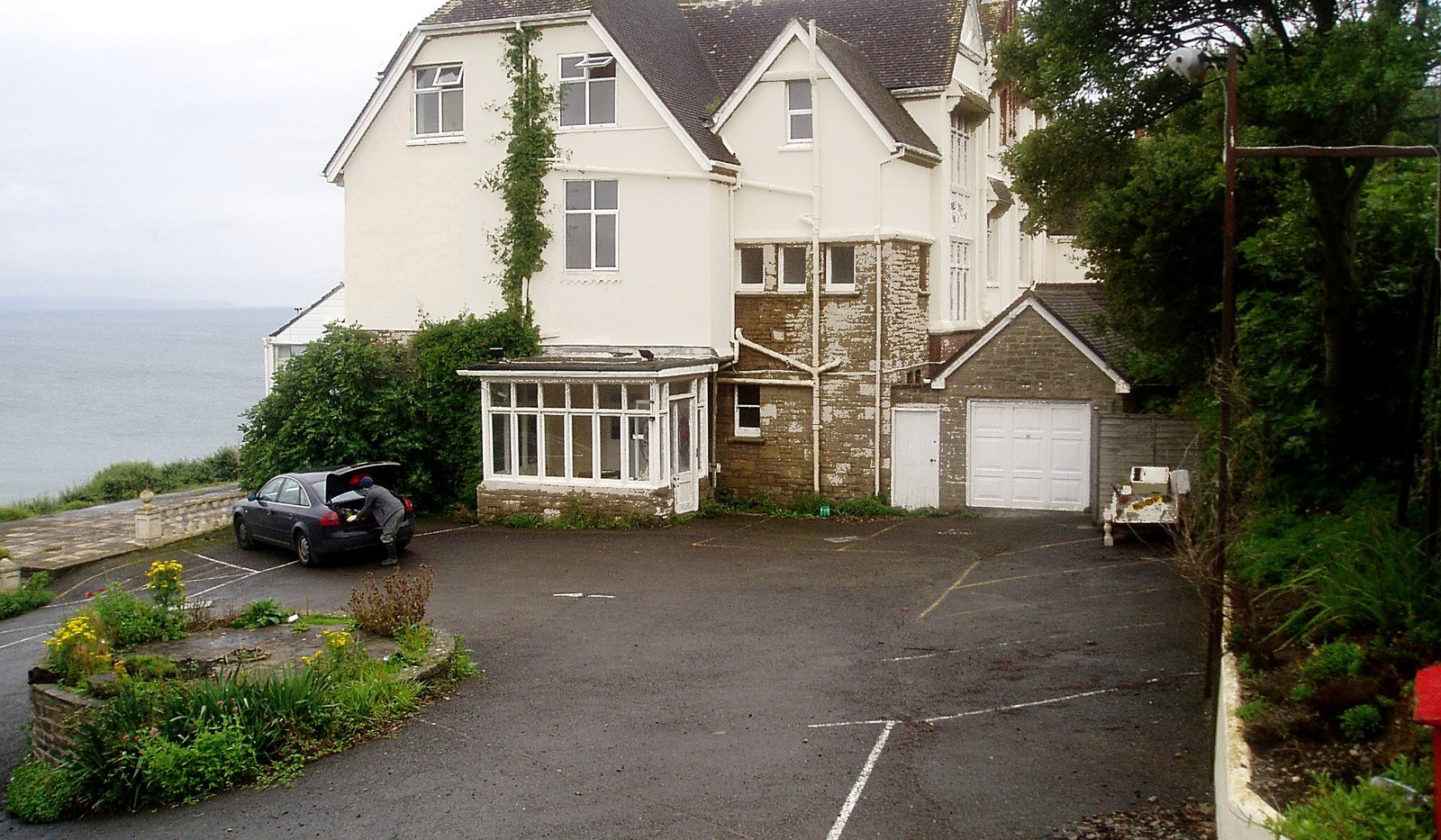 Photograph of the former Preston House Hotel as found in 2007: an ageing, ivy-clad rendered hotel building and its tarmac car park on the clifftop at Saunton, the sea beyond