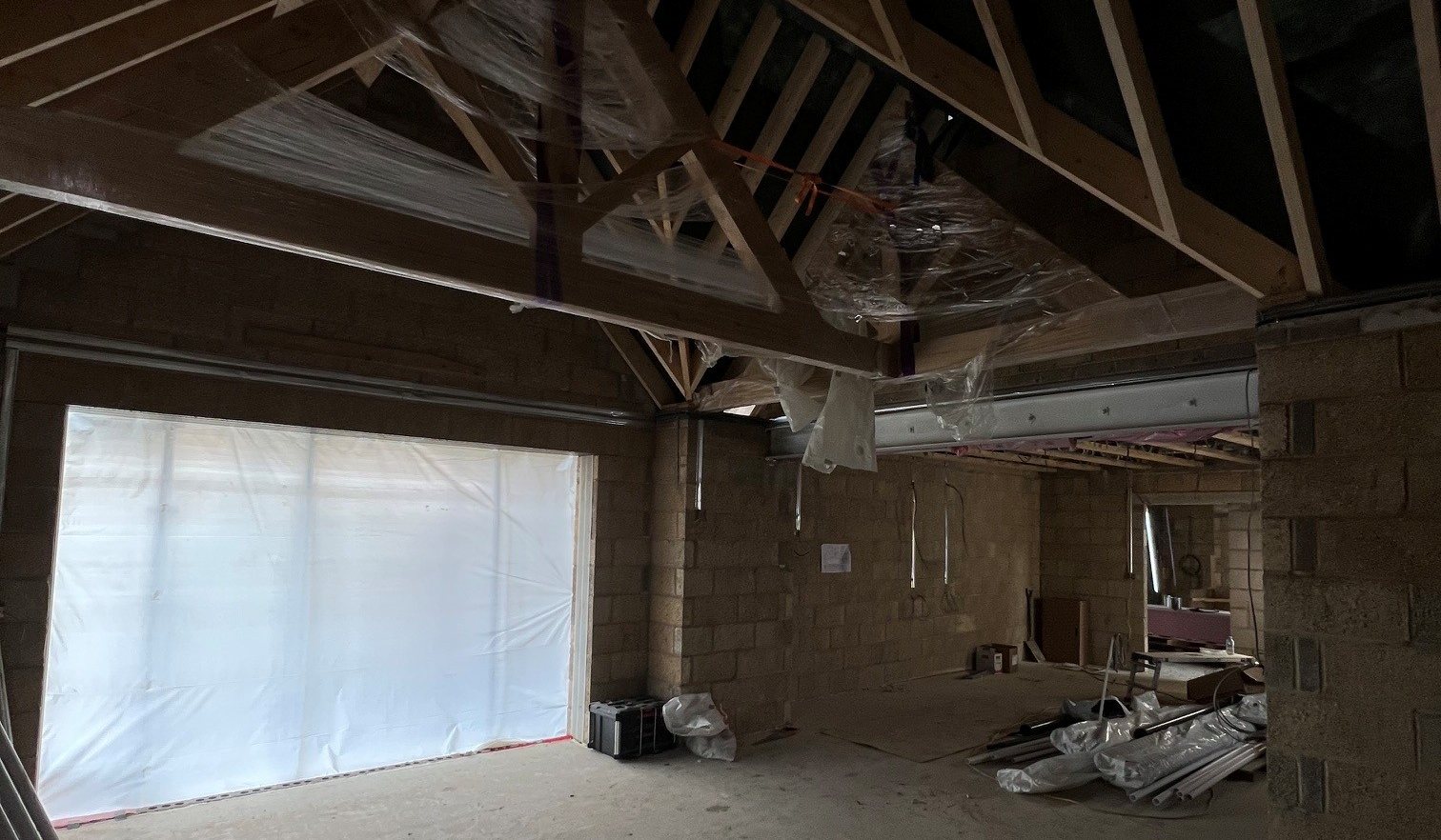An oak king-post truss with pegged joints and oak purlins erected over the vaulted family room of Hollow Meadow Farmhouse during construction, seen from inside the blockwork shell before the roof was closed
