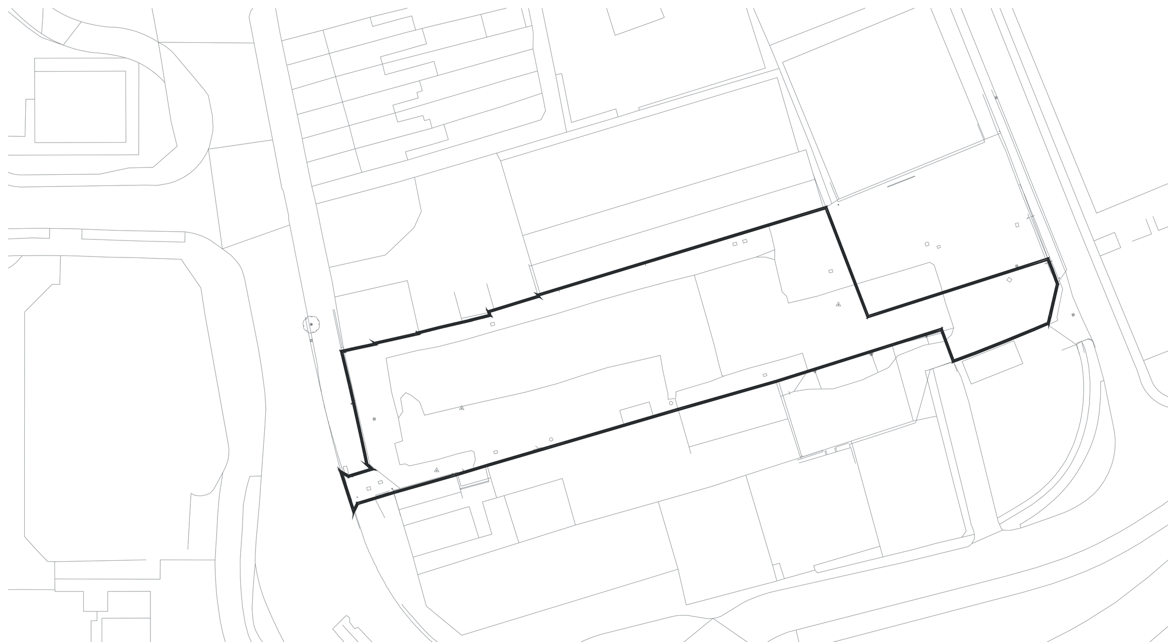 Existing site plan drawn as fine lines with no labels: a long narrow site boundary picked out in a heavier line, running diagonally between the footprints of neighbouring industrial buildings, with yards, access roads and a curving road edge drawn faintly around it