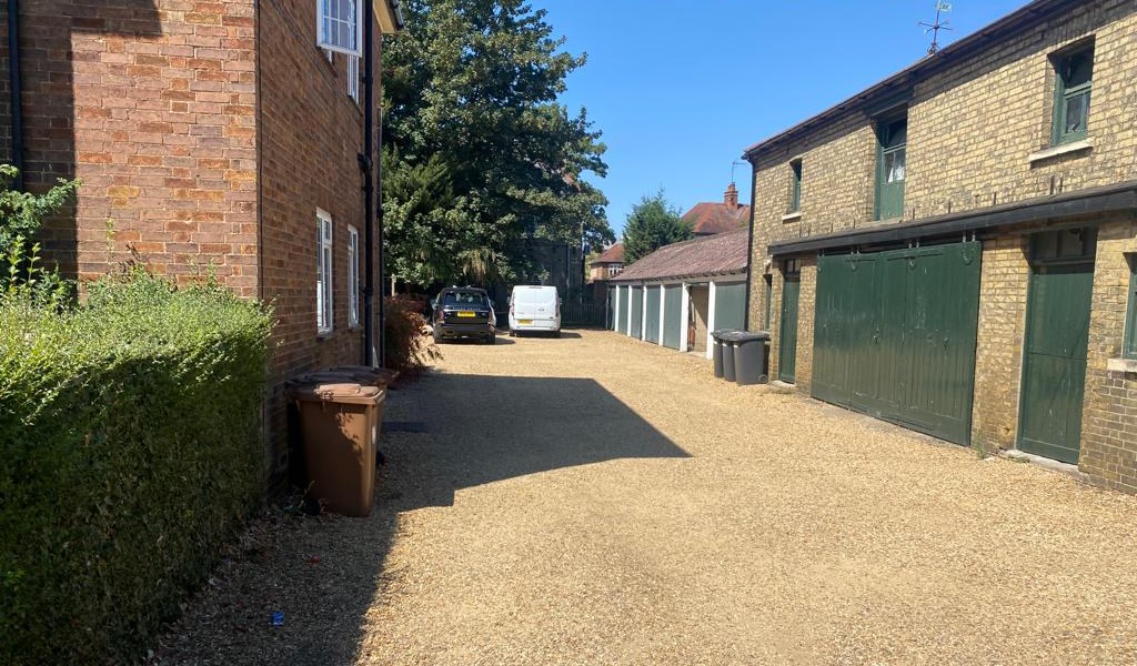 The gravel courtyard at Burghley Mansions photographed in August 2022, with the mansion block on the left and the coach house and garage range on the right