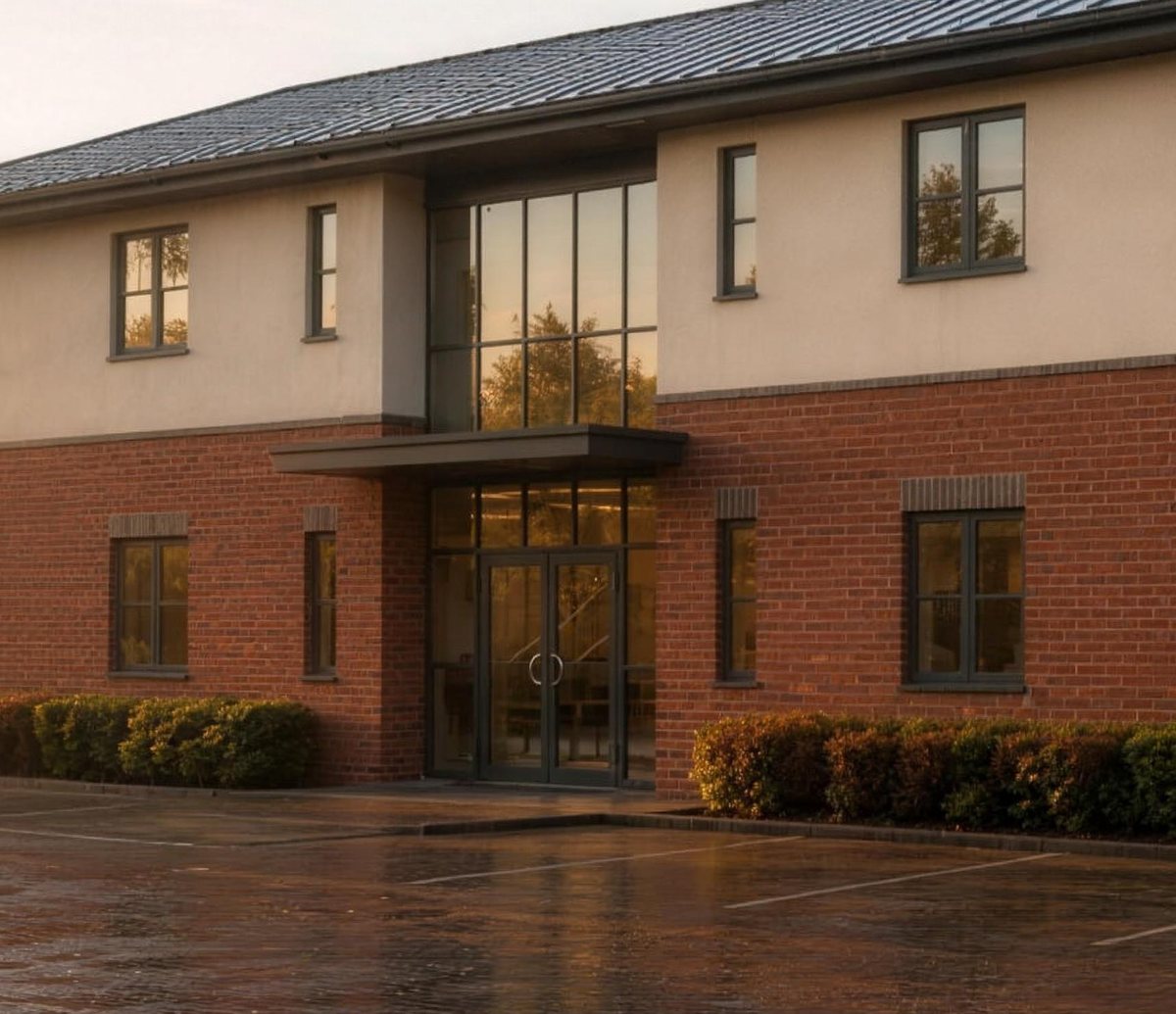 Visualisation of the consented Avonbury office seen closer in: the full-height glazed entrance bay with its canopy at the centre of the facade, brick to the ground floor and render above, with clipped hedging along the frontage