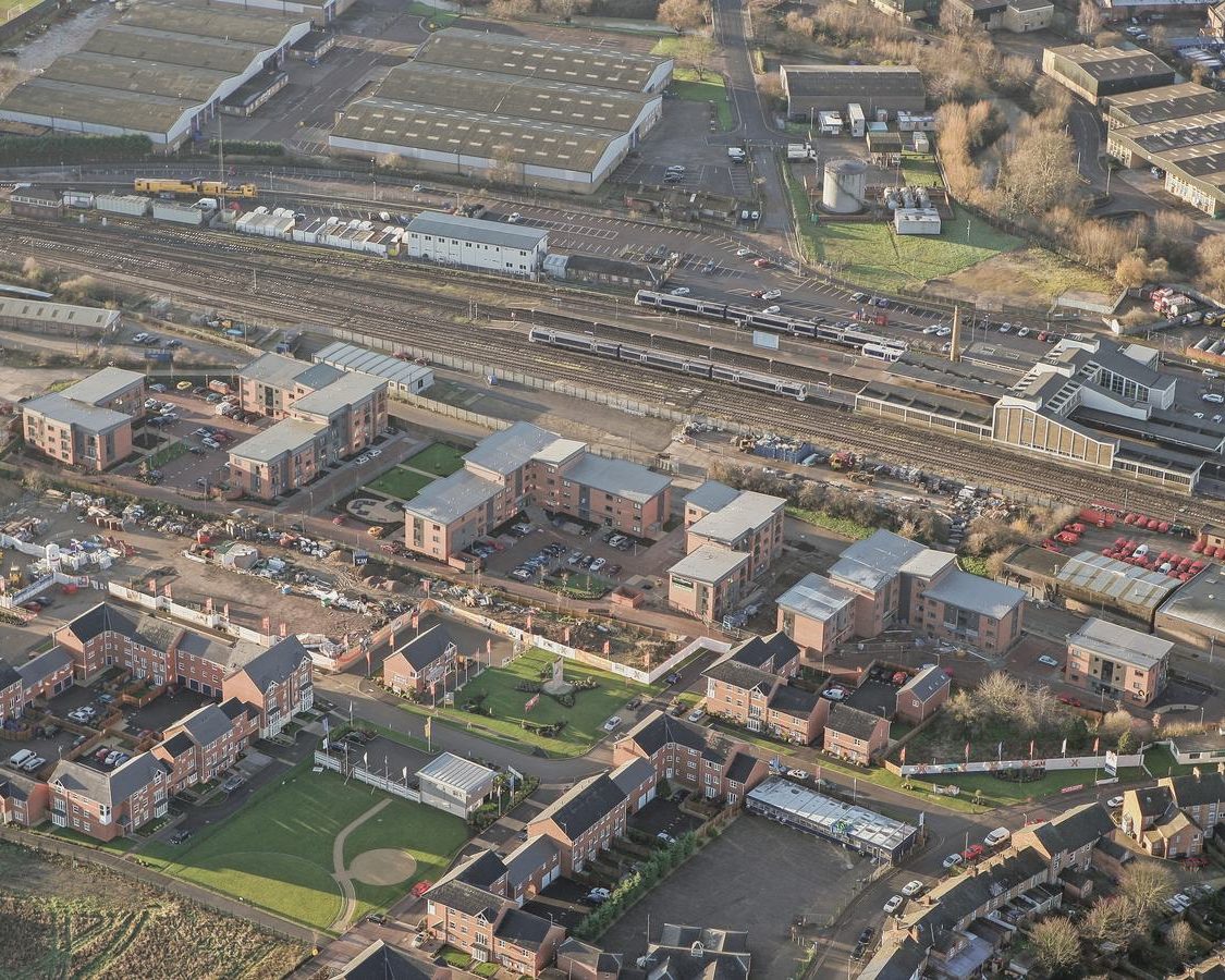Aerial photograph of the completed Market Quarter scheme on Merton Street, Banbury: the brick apartment blocks stepped along the spine of the former cattle market, with the mainline railway and the station alongside.