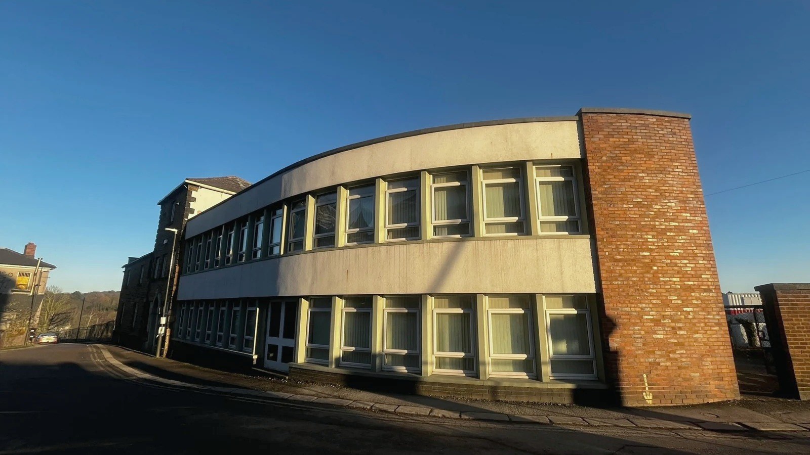 37 Station Road, Chesterfield as it stands: a part two, part three-storey former office with its 19th-century stone range at the left and a later curved rendered frontage with a red-brick stair tower, on a plot running as a surface car park