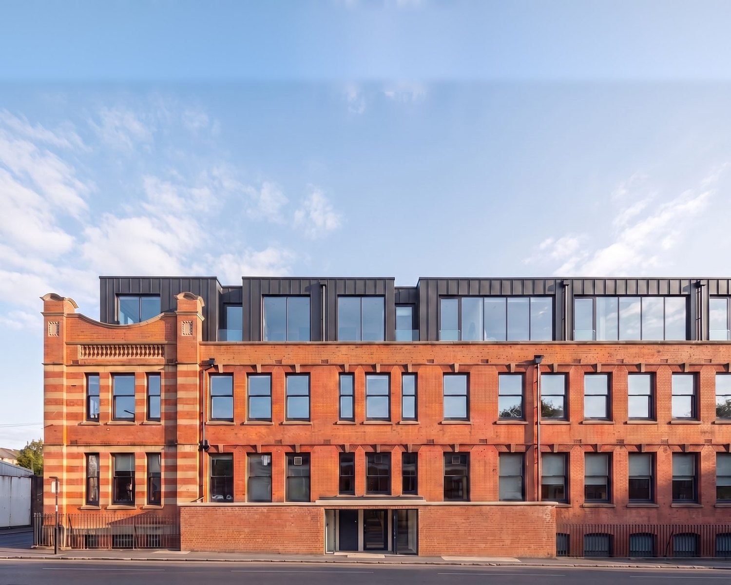 An enhanced photograph of the converted 1906 Former Challenge Cycle Works at Foleshill Road, Coventry: the retained red brick and terracotta facade with its ornate gable below the new dark zinc-clad top storey added by the conversion.