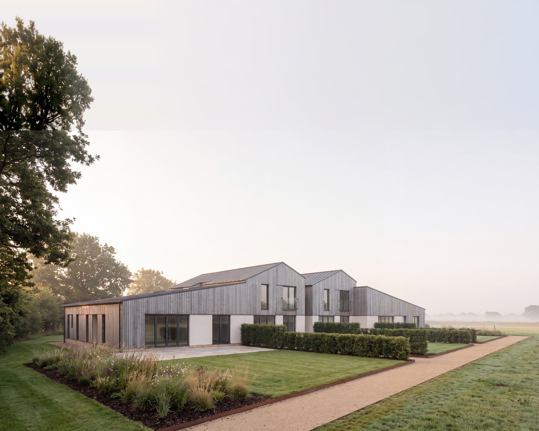 Visualisation of a converted South Warwickshire fertiliser barn: a long, low range in silver-grey vertical larch with two gables, seen across the garden on a misty morning.