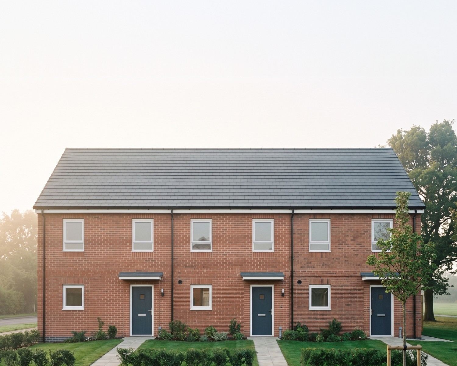 Visualisation of the consented scheme at Hopwood, Bromsgrove: a terrace of homes for social rent in two red multi bricks with an engineering brick plinth, projecting brick panels, brick soldier lintels over the openings, white windows and a slate grey interlocking tiled roof.