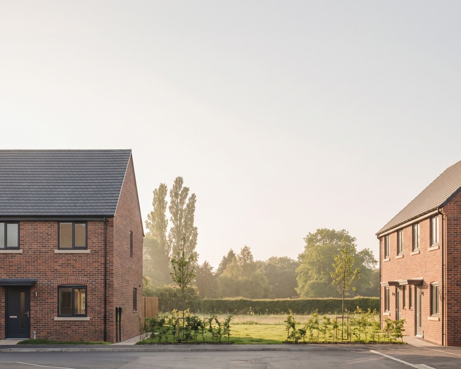 Visualisation of the consented scheme at Picken End, Hanley Swan: semi-detached pairs of affordable homes in brindle brick with segmental brick arches, stone cills and grey tiled roofs, either side of the new estate road, with the retained hedgerow and meadow beyond.