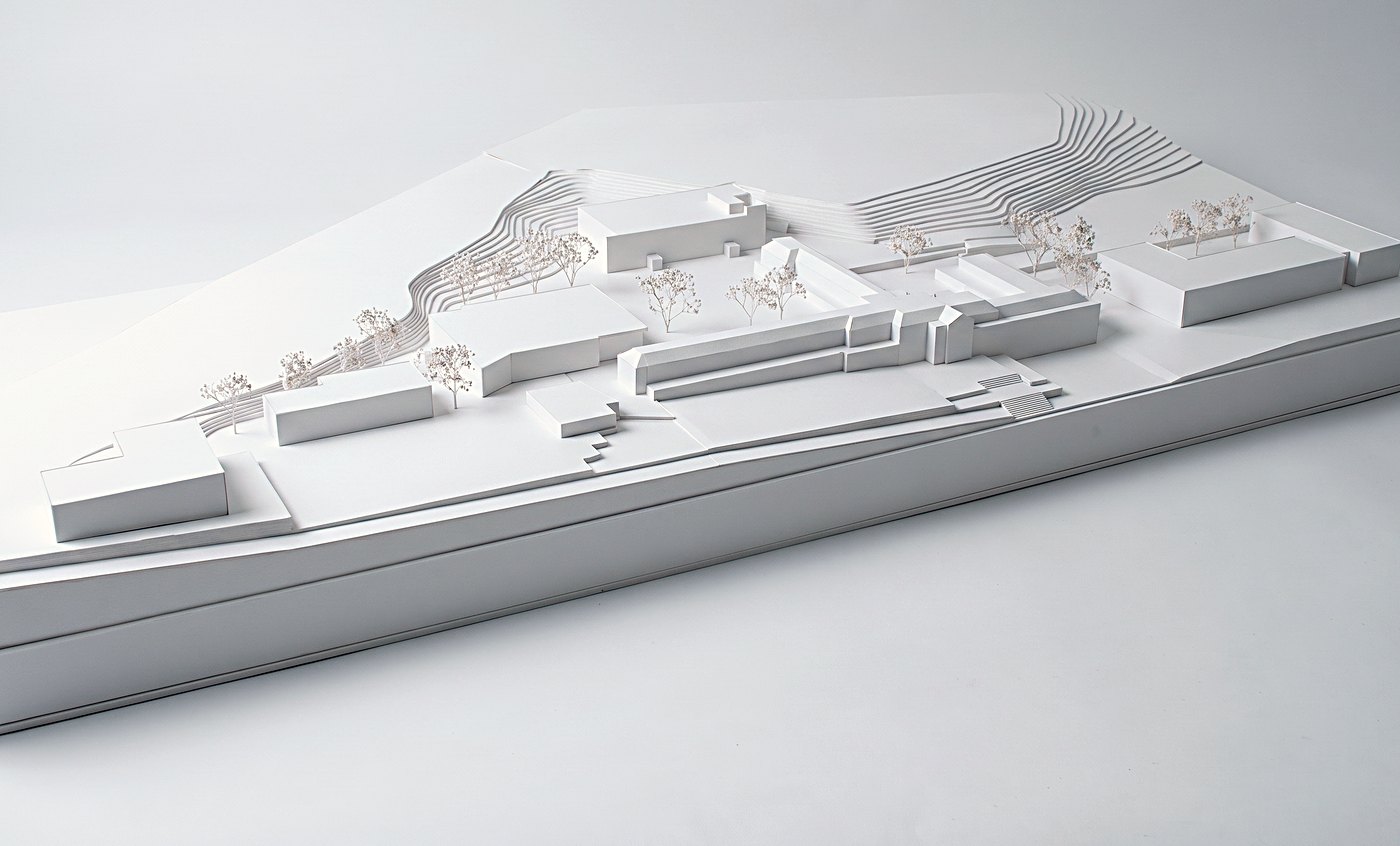 Rickett Architects study model of the Oxford Business College campus masterplan, Nottingham, seen from a raised three quarter angle: the run of white college buildings stepped along the plinth, the amphitheatre terracing cut into the slope behind, and fine model trees across the campus
