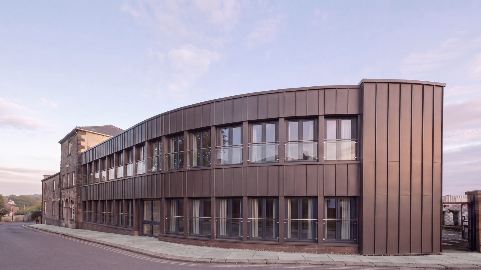 An indicative impression of 37 Station Road, Chesterfield brought back into use as apartments: the later curved frontage and stair tower reclad in dark bronze standing-seam metal, the retained 19th-century stone range restored, seen from the Station Road approach