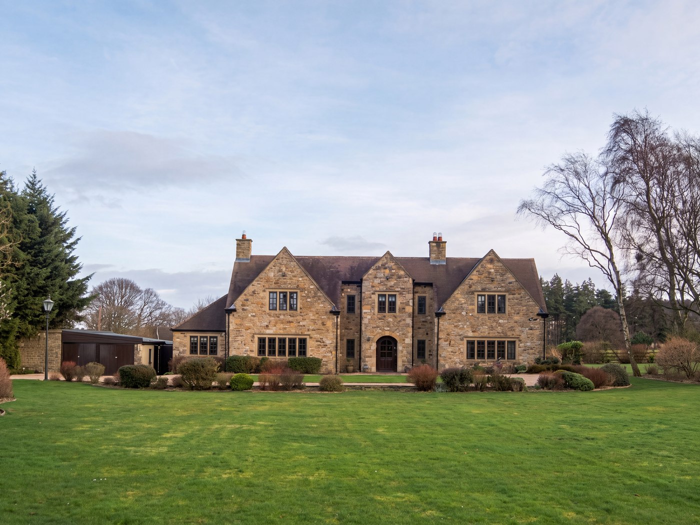 The country house before the works: two storeys of coursed local stone with gabled bays, behind a wide lawn