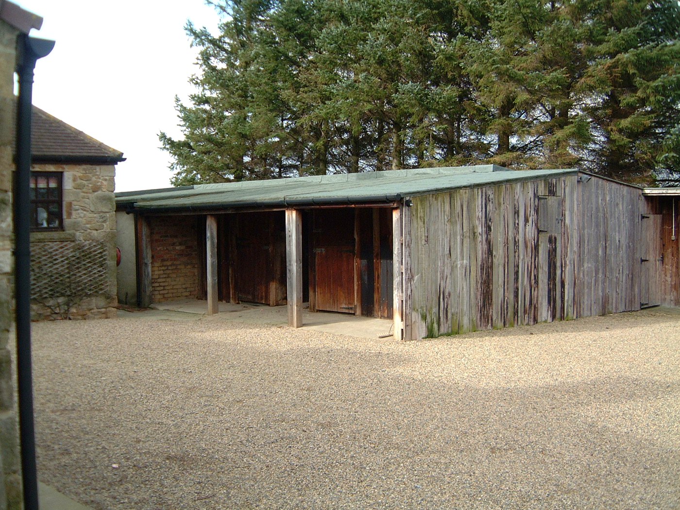 The dilapidated timber outbuildings before the works: weathered sheds with a sagging roof behind the house