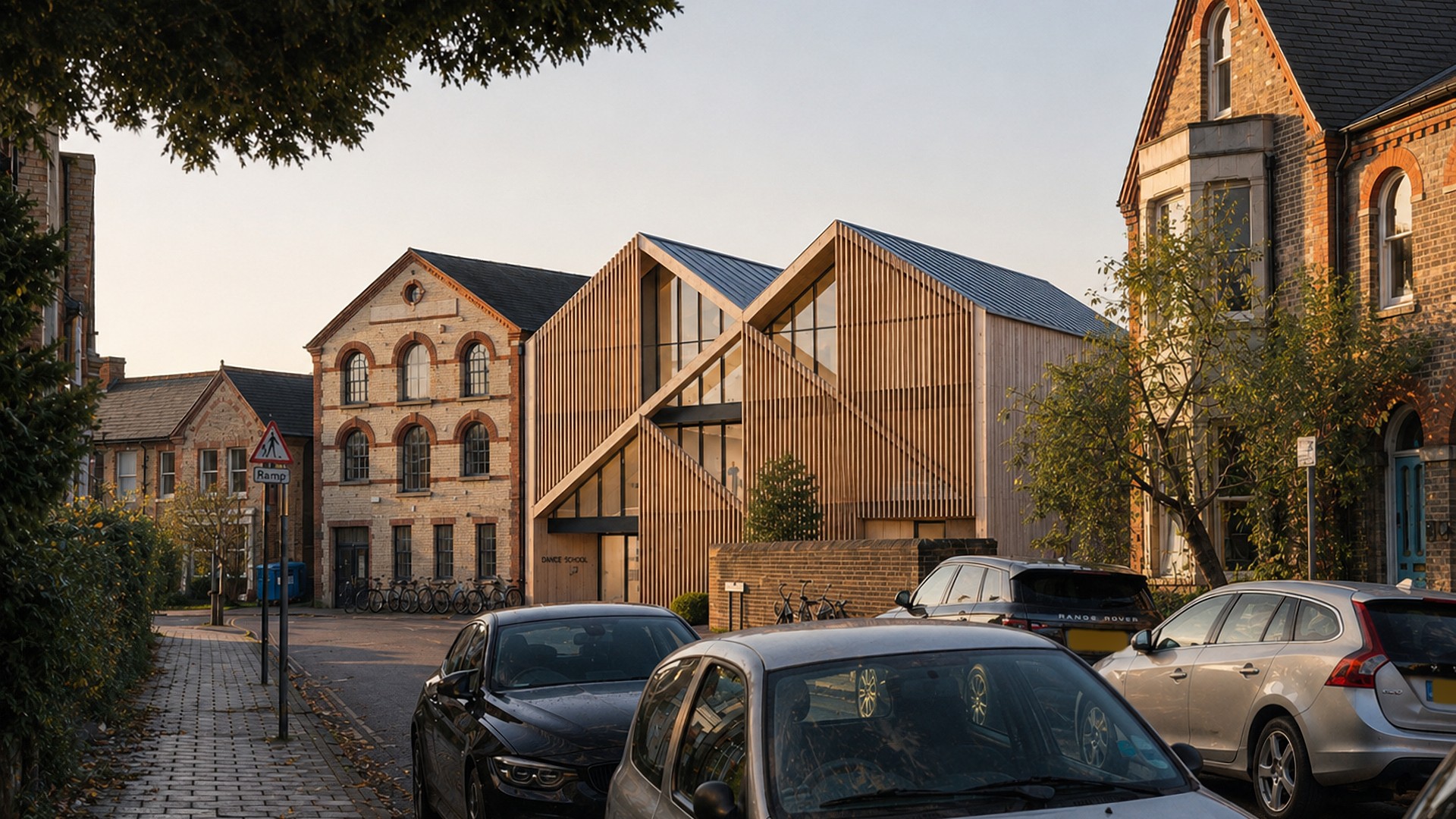 A Rickett Architects visualisation of the massing tested in the feasibility study: a timber-screened building with two pitched gables set between a retained brick dance school and the neighbouring houses on a Cambridge street, in low warm light