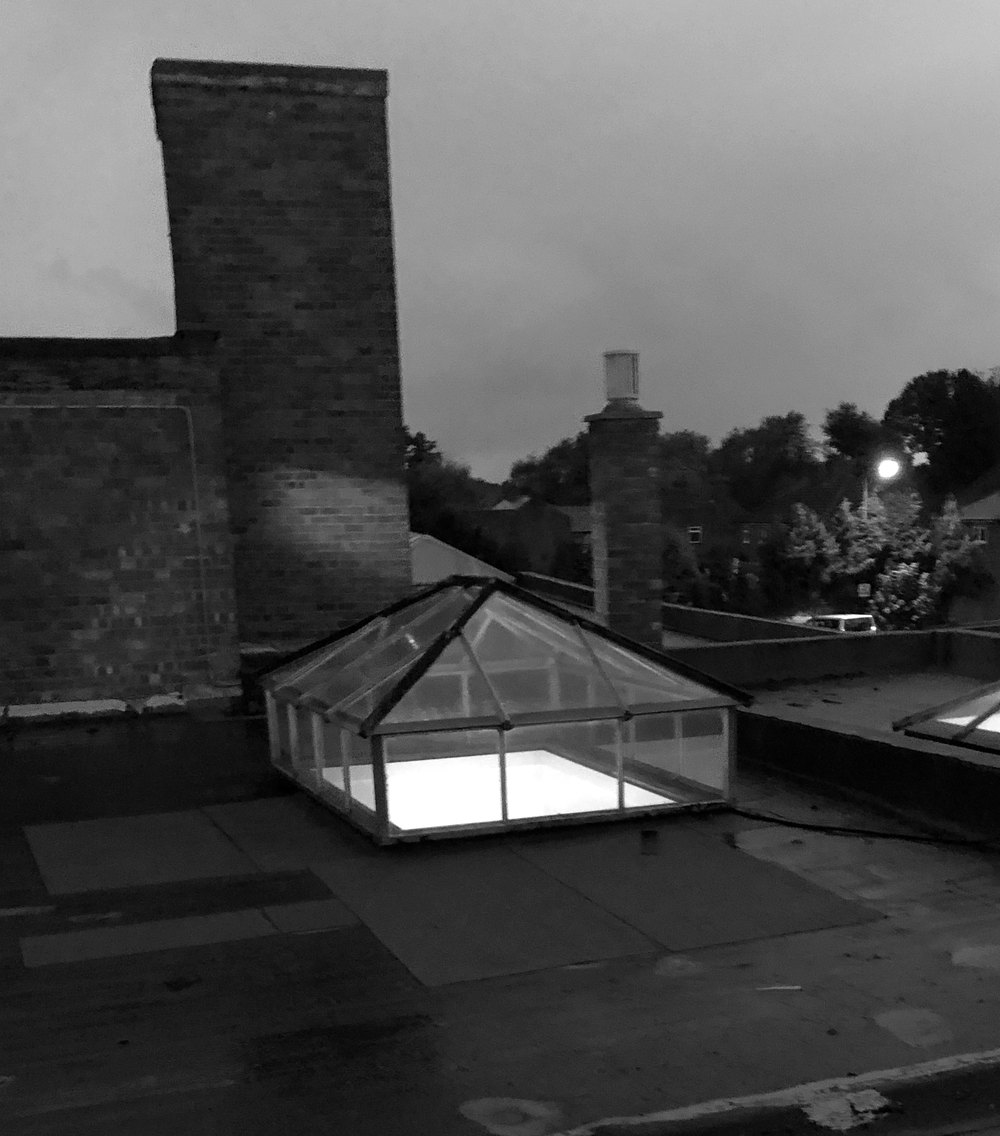 Black and white photograph of the store's flat roof at dusk in October 2019, with two roof lanterns