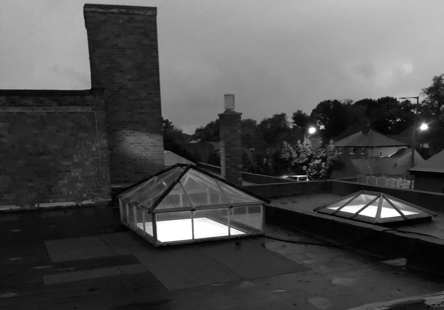 Black and white photograph of the store's flat roof at dusk in October 2019, with two roof lanterns