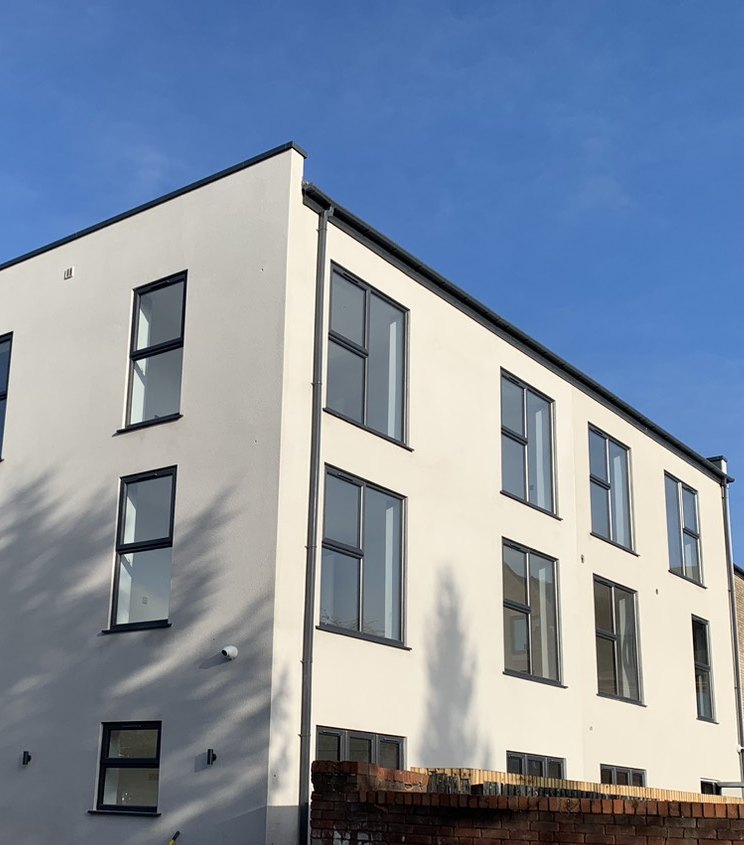 Photograph of the rear in December 2022: a three-storey white rendered block with dark grey windows