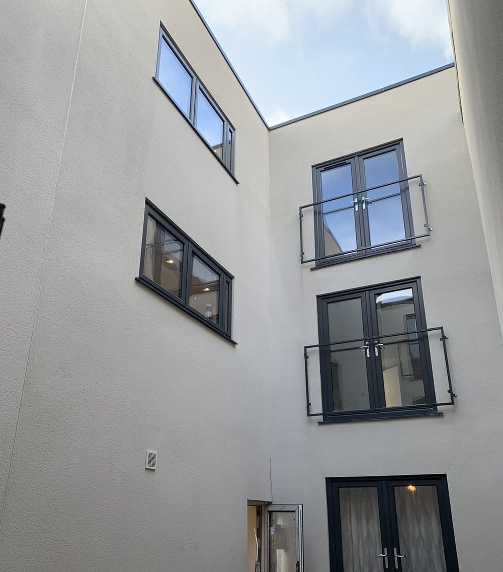 Photograph looking up a light well in December 2022: white render, French doors and Juliet balconies