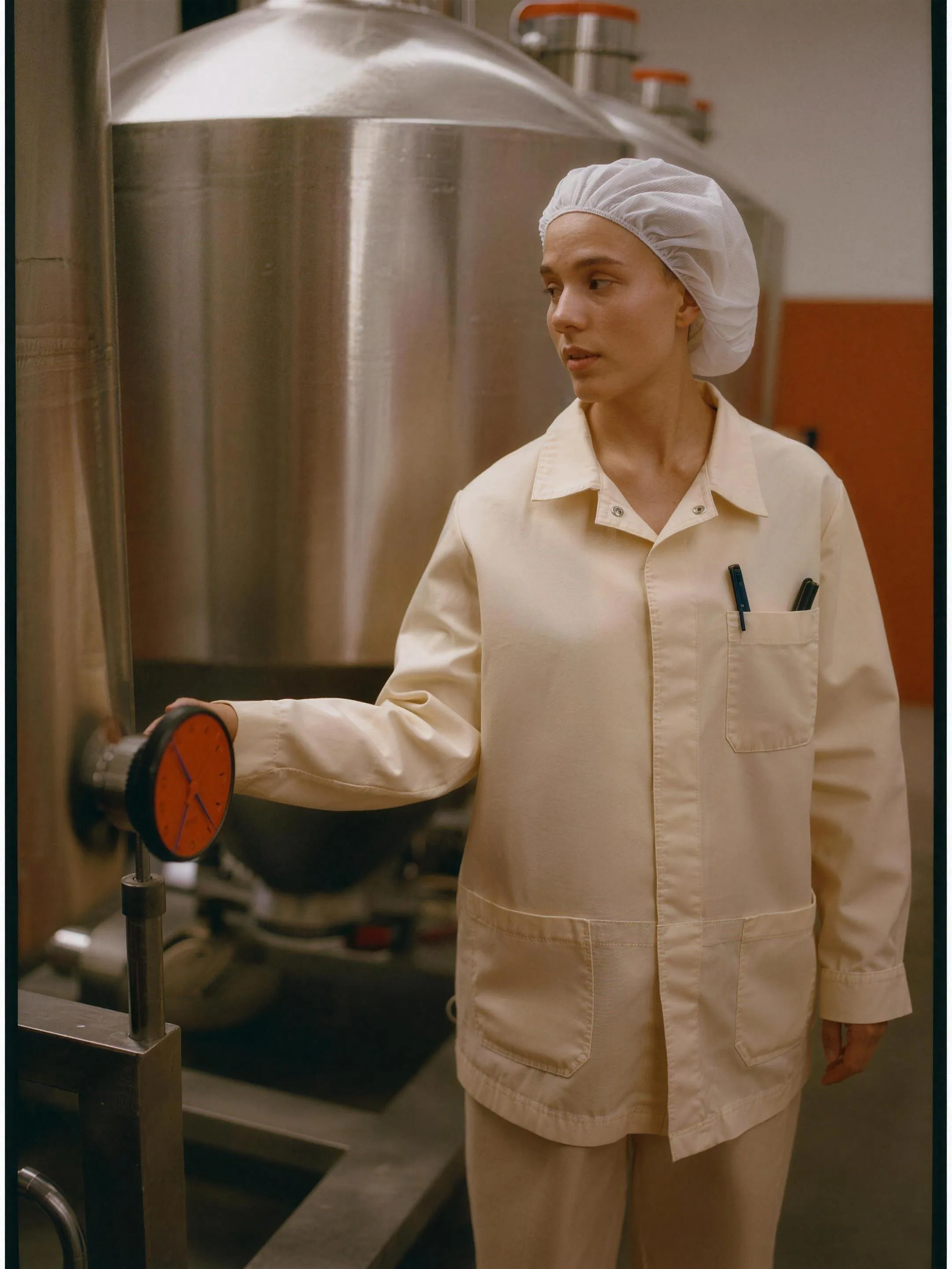 Technician in a hairnet beside stainless steel processing tanks