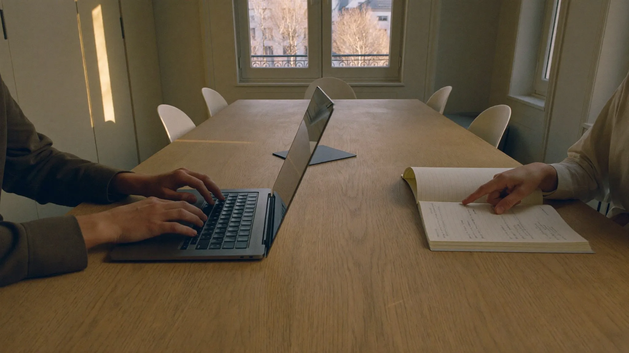 Two consultants working across a meeting table with a laptop and notebook