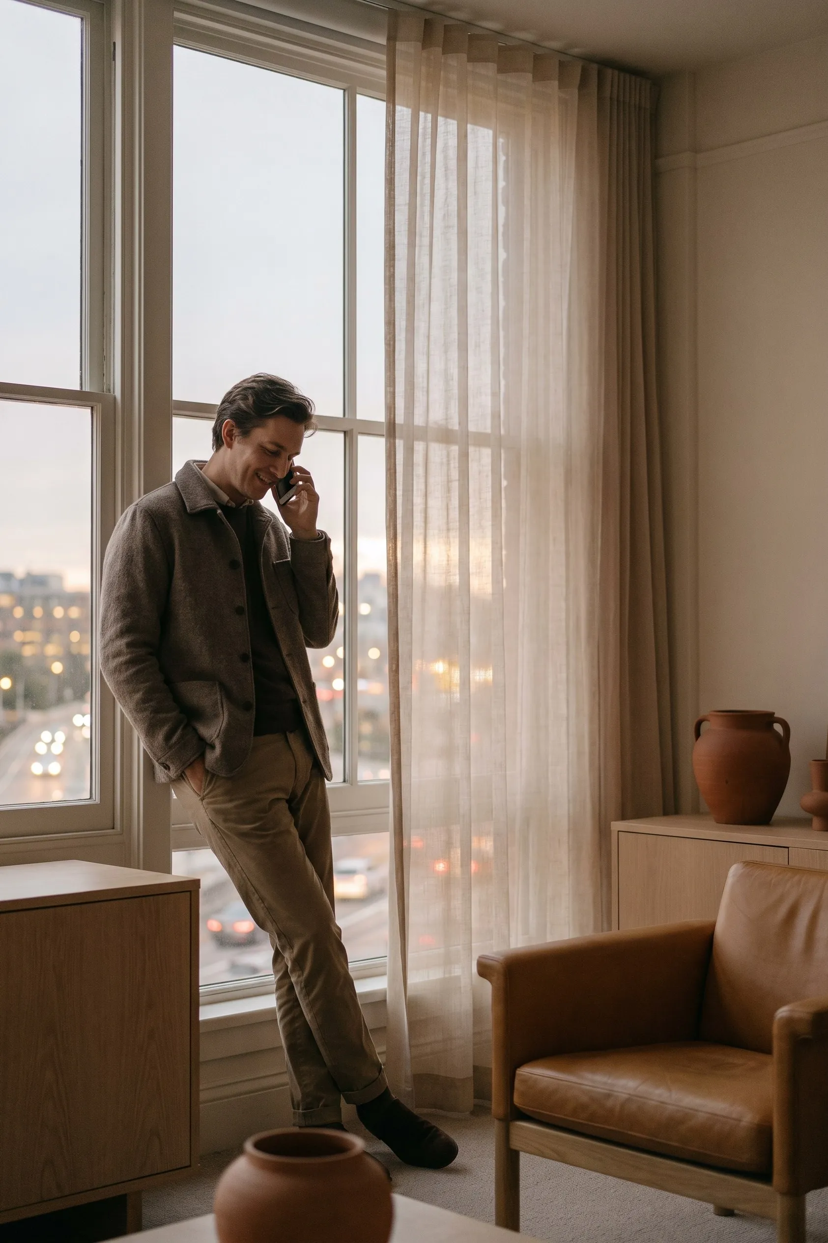 Person standing at a window in a warm office, taking a phone call