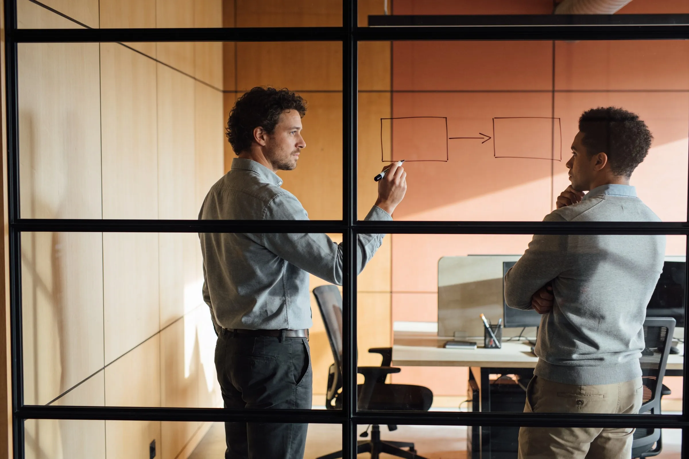Two engineers working through a system architecture drawn on a glass partition
