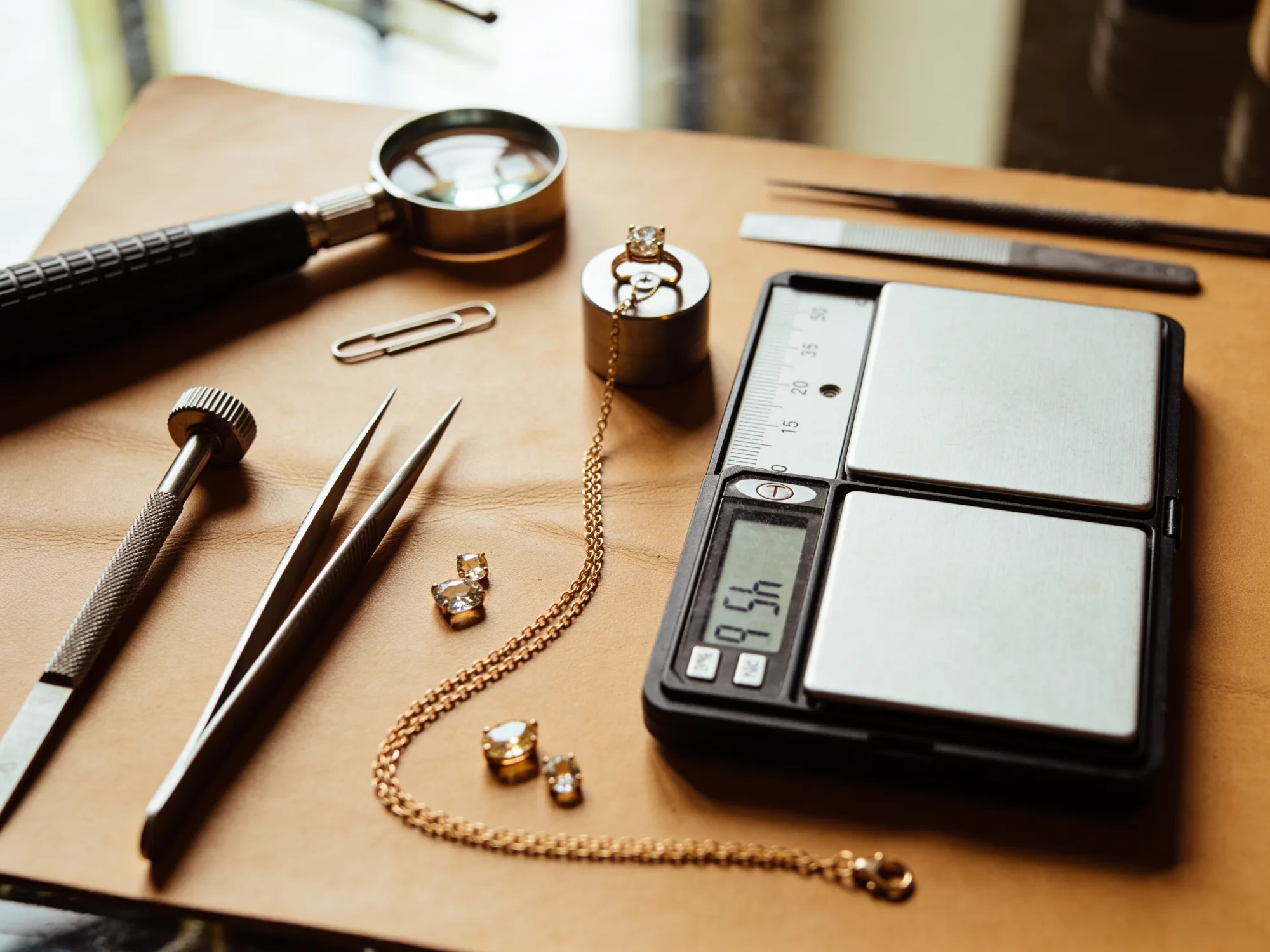 Jewelry repair station with tweezers, a loupe, a scale, and a gold chain