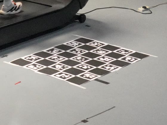 ChArUco calibration board lying flat on the studio floor, each white square carrying an ArUco marker