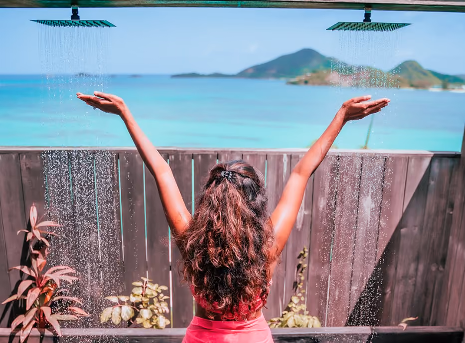 Guest enjoying an outdoor shower surrounded by tropical planting with sea views