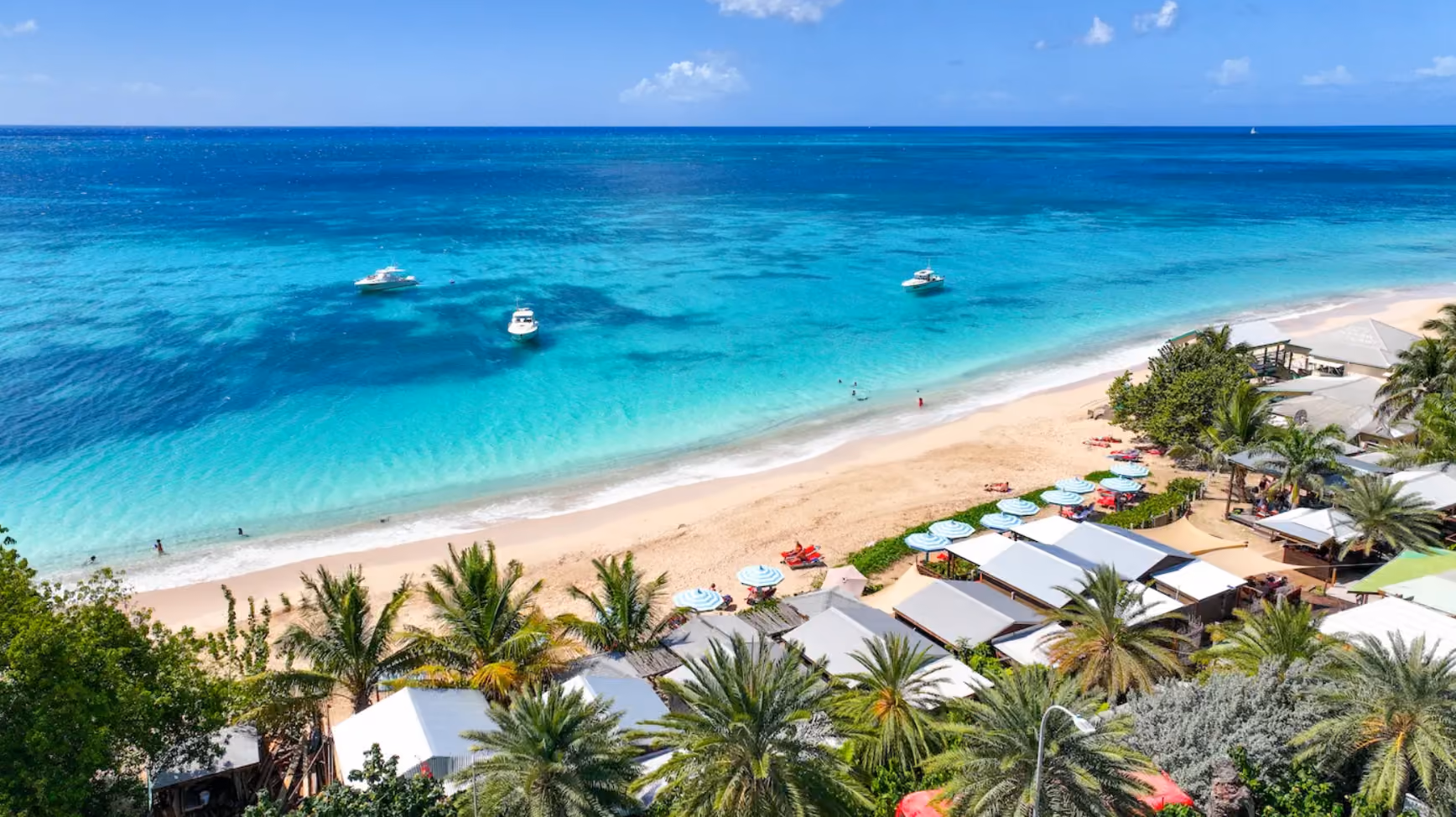Beach cabins and umbrellas on a white sand beach with boats moored offshore