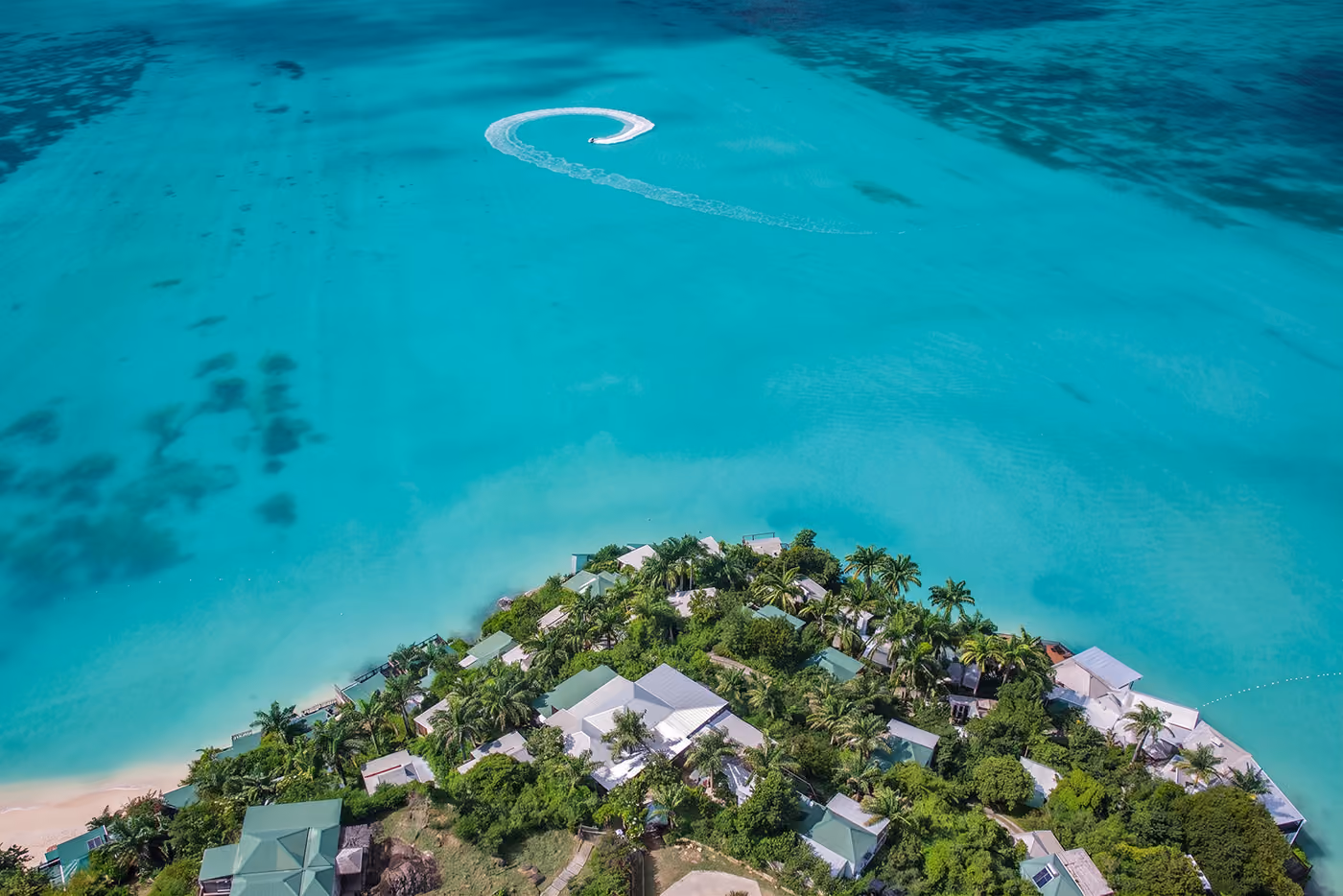 Aerial view of Cocos Hotel cottages on a palm-covered headland above turquoise sea, Antigua
