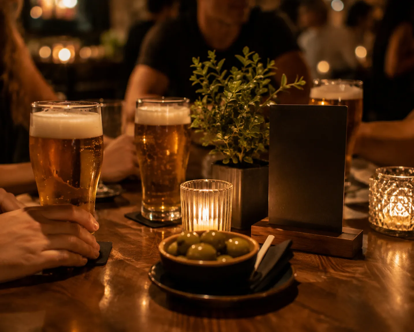 Verres de bière sur une table en bois avec bol d'olives, bougies et plante en pot dans un bar.
